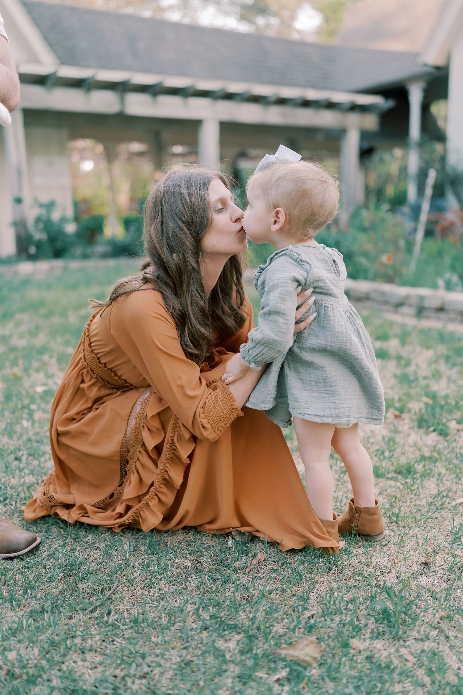 A tender moment captured on grass with a flowing rust-colored dress in the foreground.