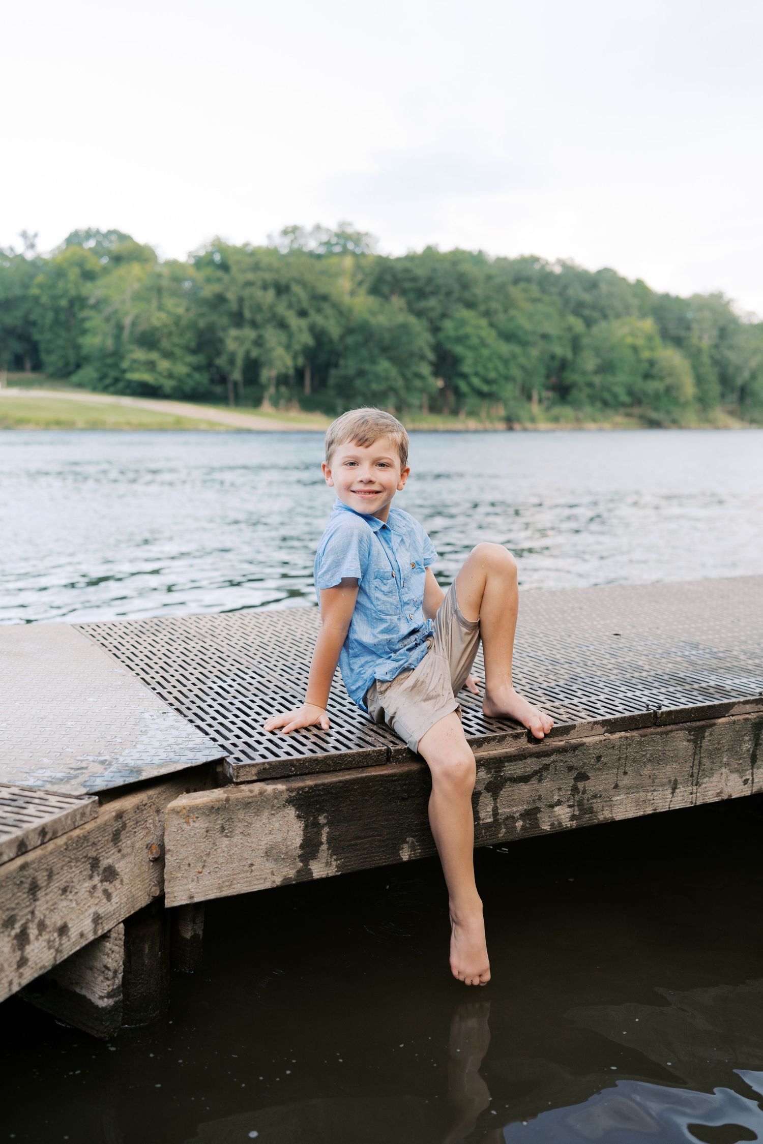 A child sits on the edge of a weathered wooden dock overlooking a serene lake.