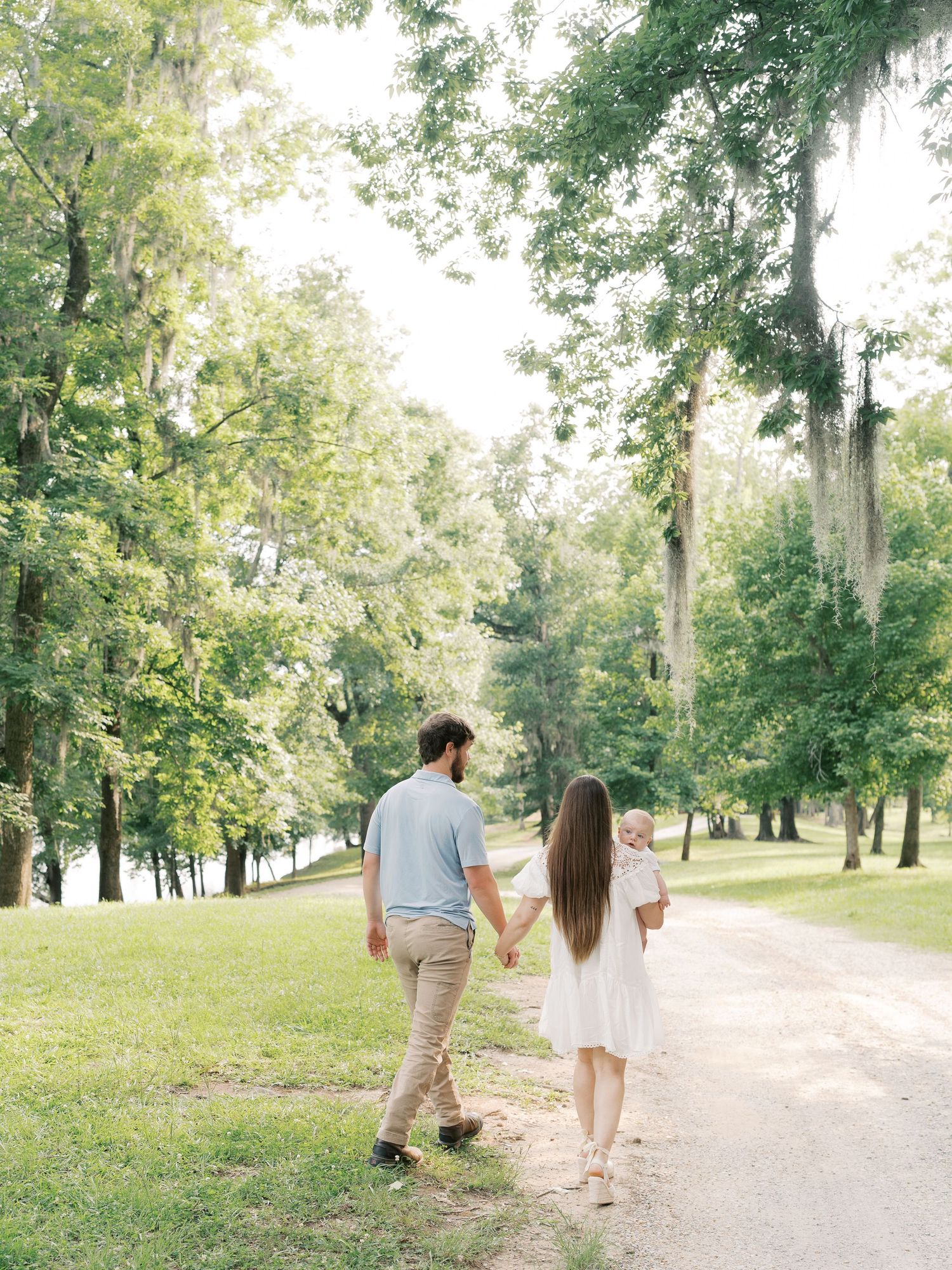 A couple walks hand in hand down a scenic park path surrounded by trees.