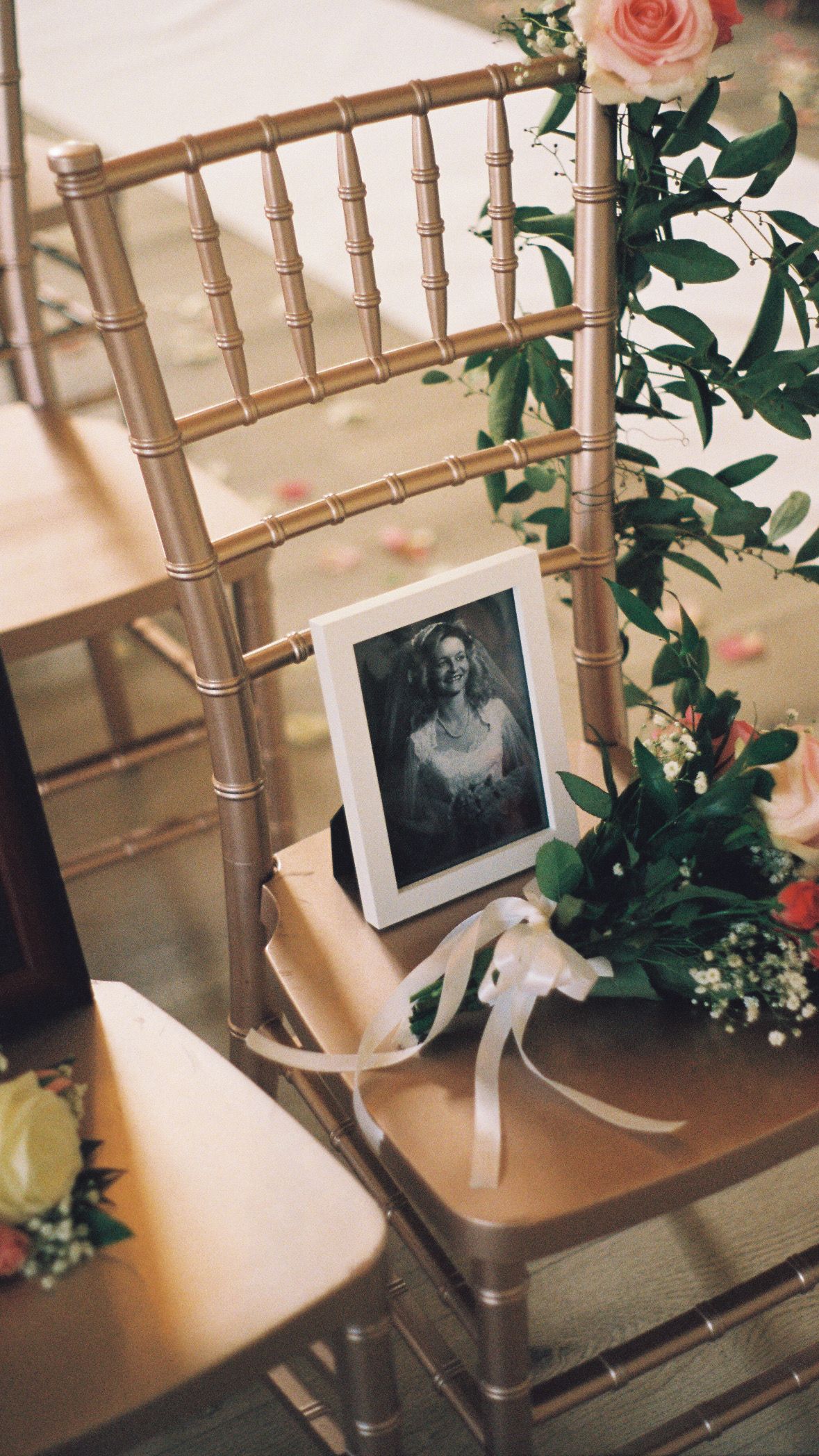 Gold Chiavari chair decorated with flowers and framed photo at wedding reception.