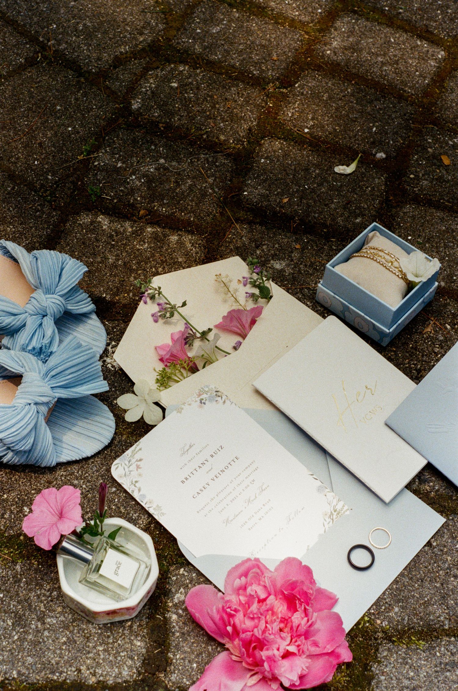 Wedding stationery with pink flowers and blue ribbons displayed on dark stone background.