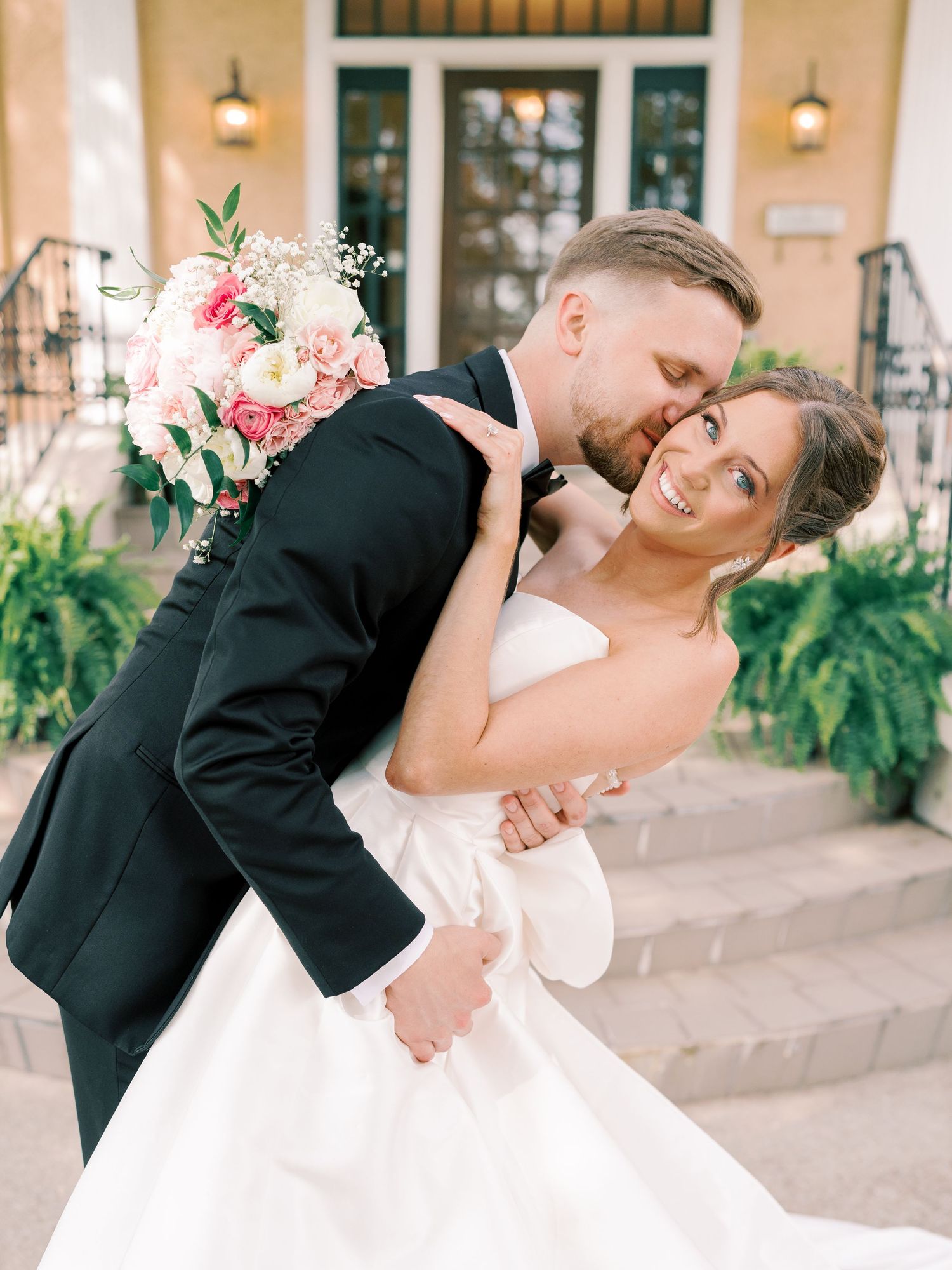 Couple in formal wedding attire sharing a romantic dip pose on stone steps.