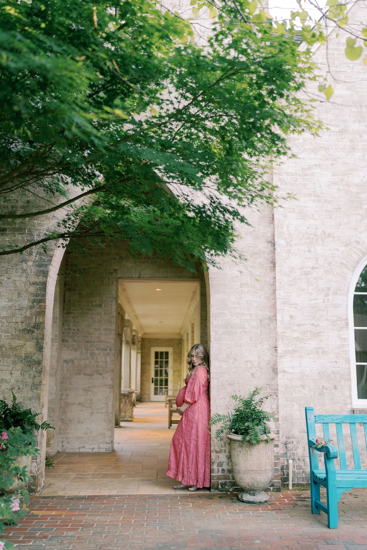 A stone building walkway with blue benches and overhanging trees creates an elegant outdoor setting.