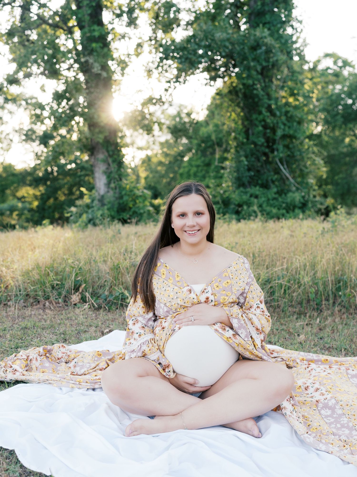Peaceful maternity session with flowing yellow dress on white blanket in outdoor setting.