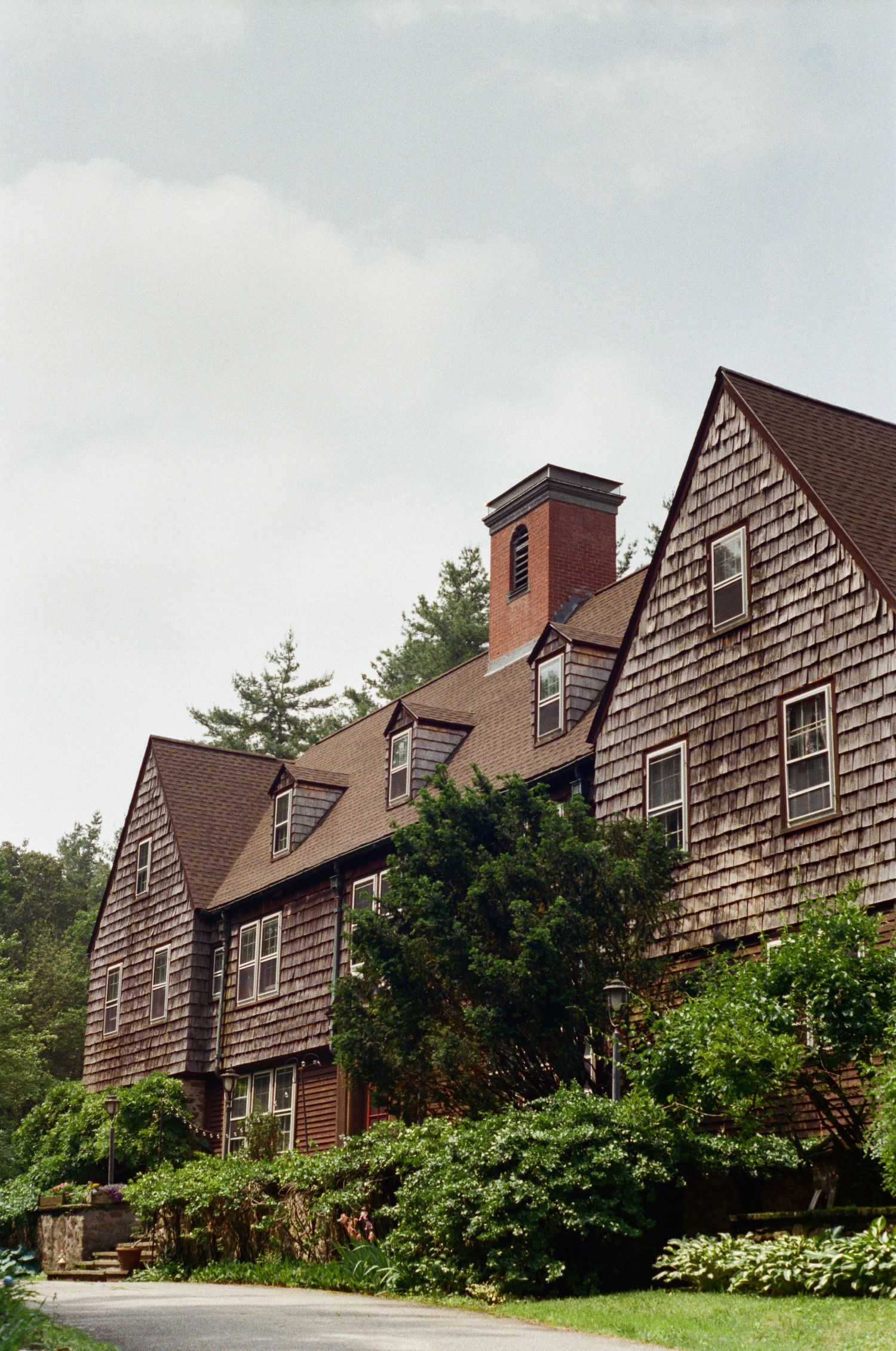 Row of rustic brown shingled houses with brick chimneys nestled among green trees and bushes.