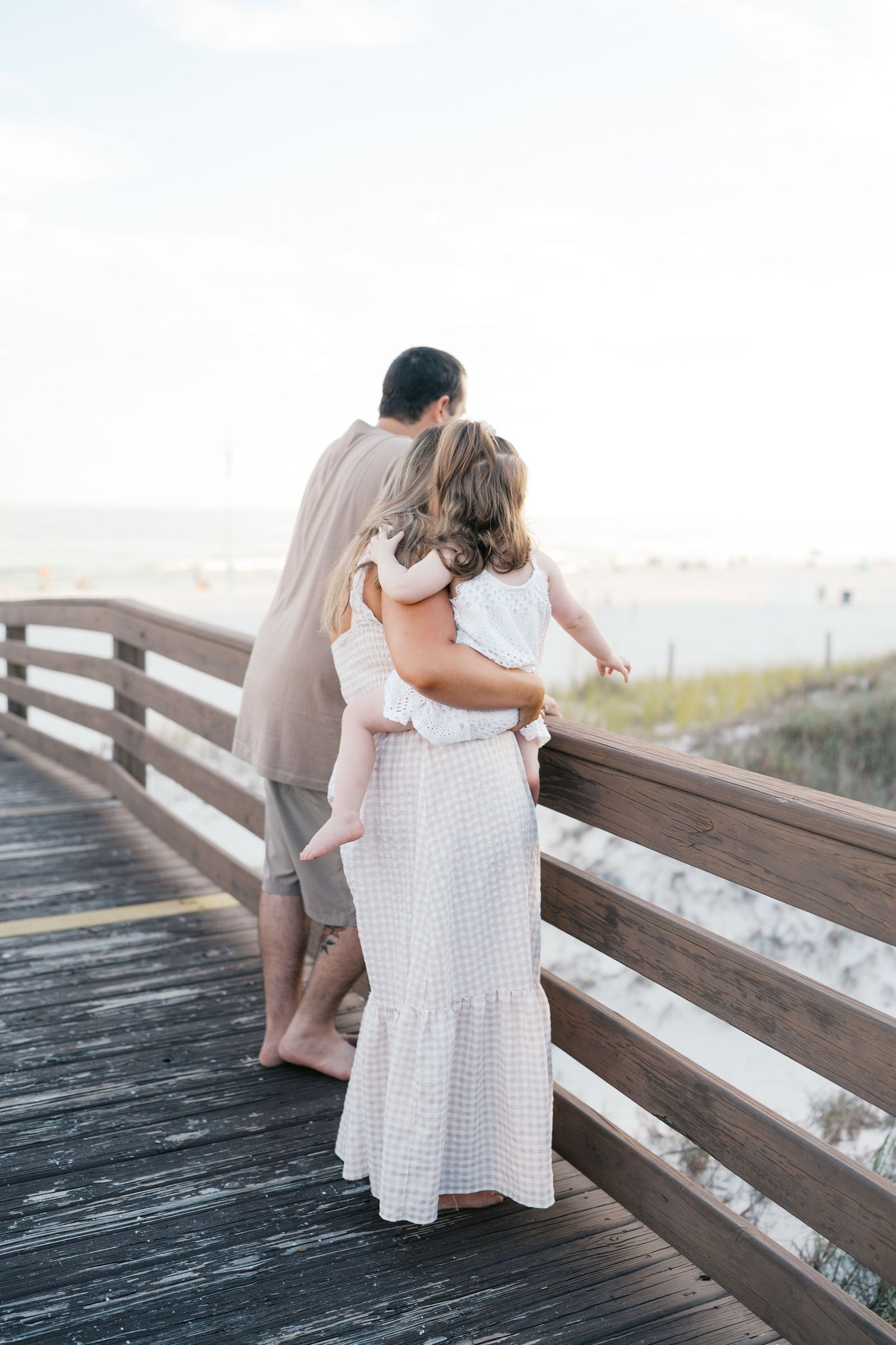Family members share tender moments on a wooden beach boardwalk.