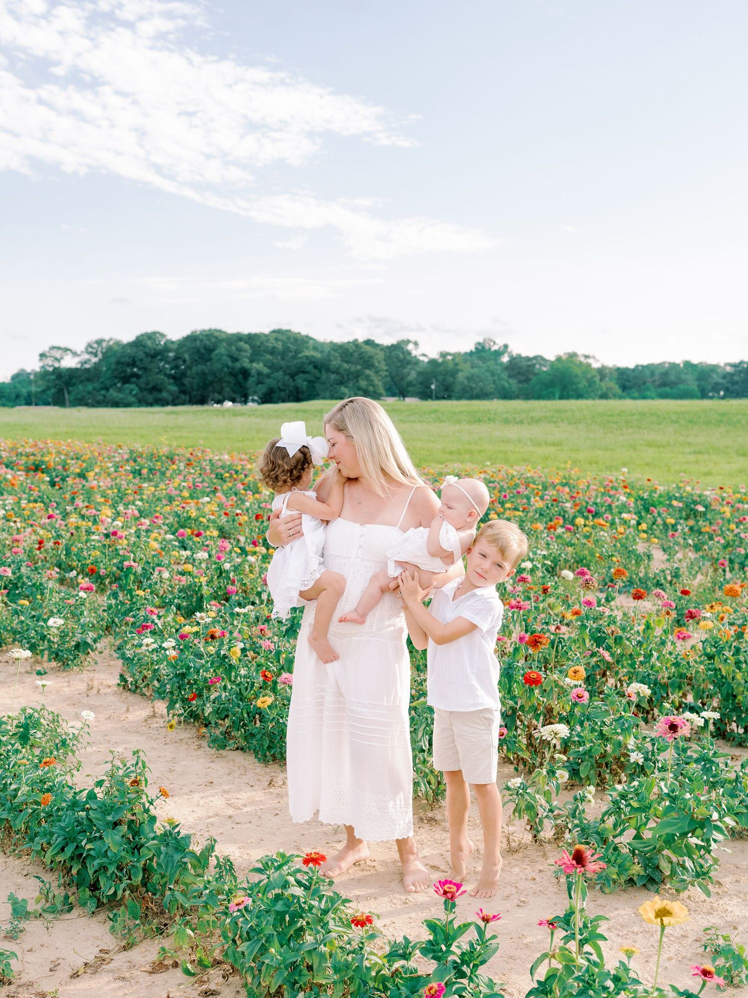 Family members in white outfits interact playfully among colorful blooming flowers.