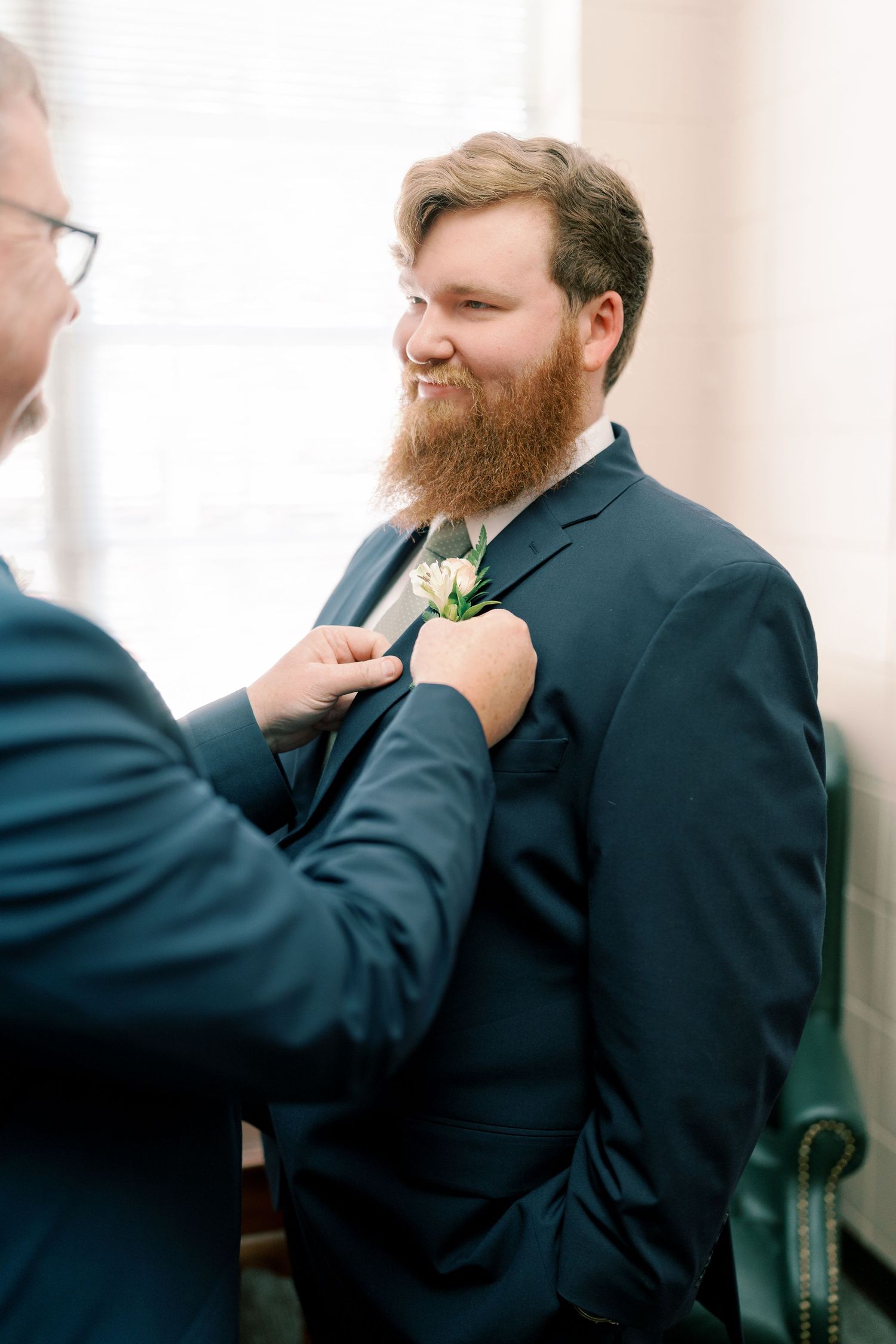 Groomsman adjusting tie and boutonniere in formal black suit.