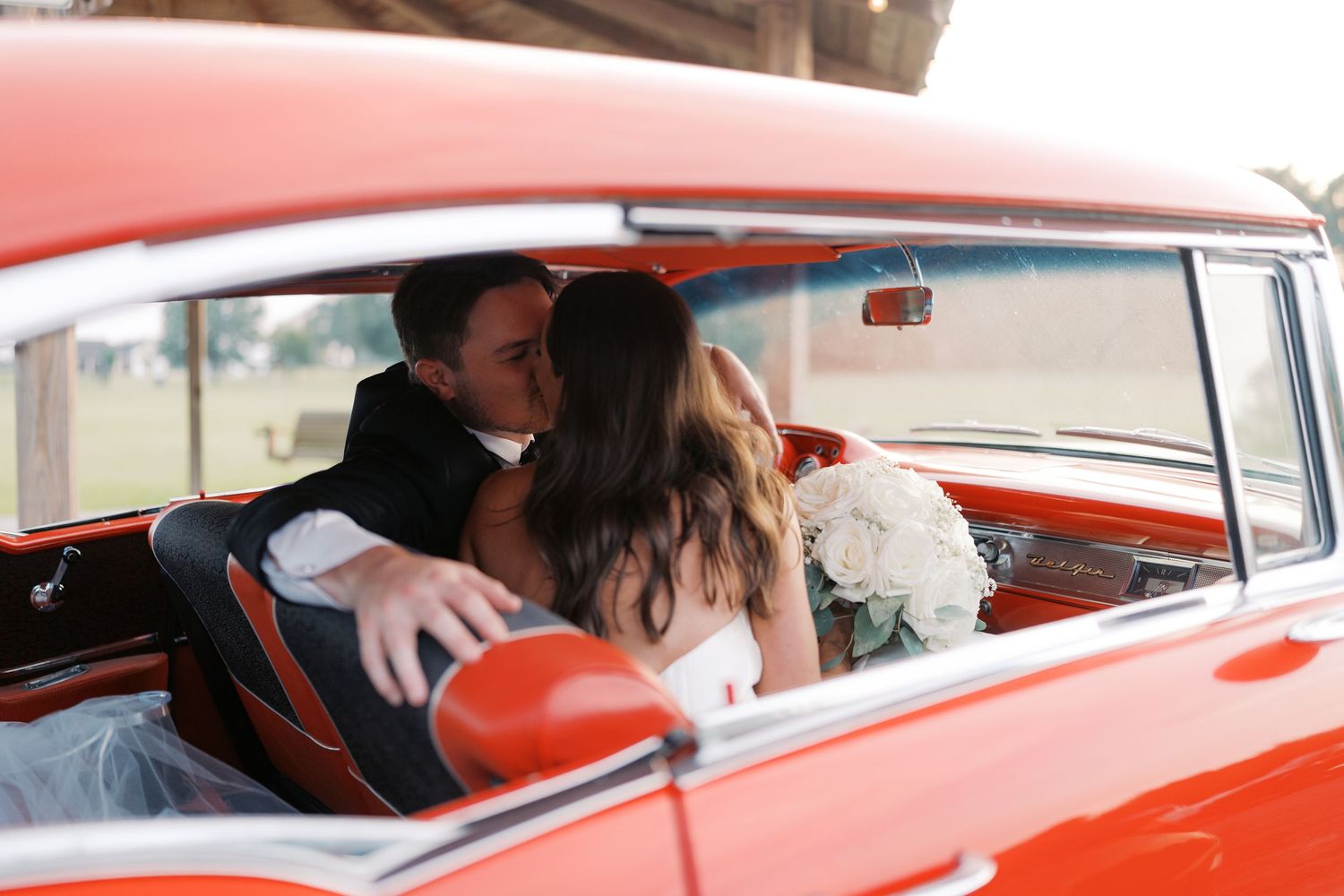 Newlyweds share intimate moments in a classic red vintage car.