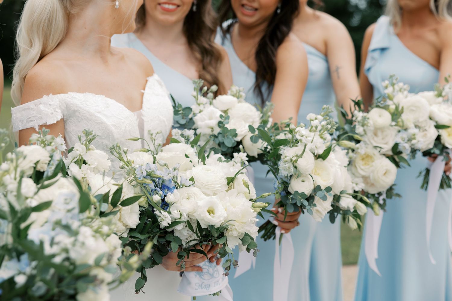 Wedding party in light blue bridesmaid dresses and cream suits holding white and green floral bouquets.