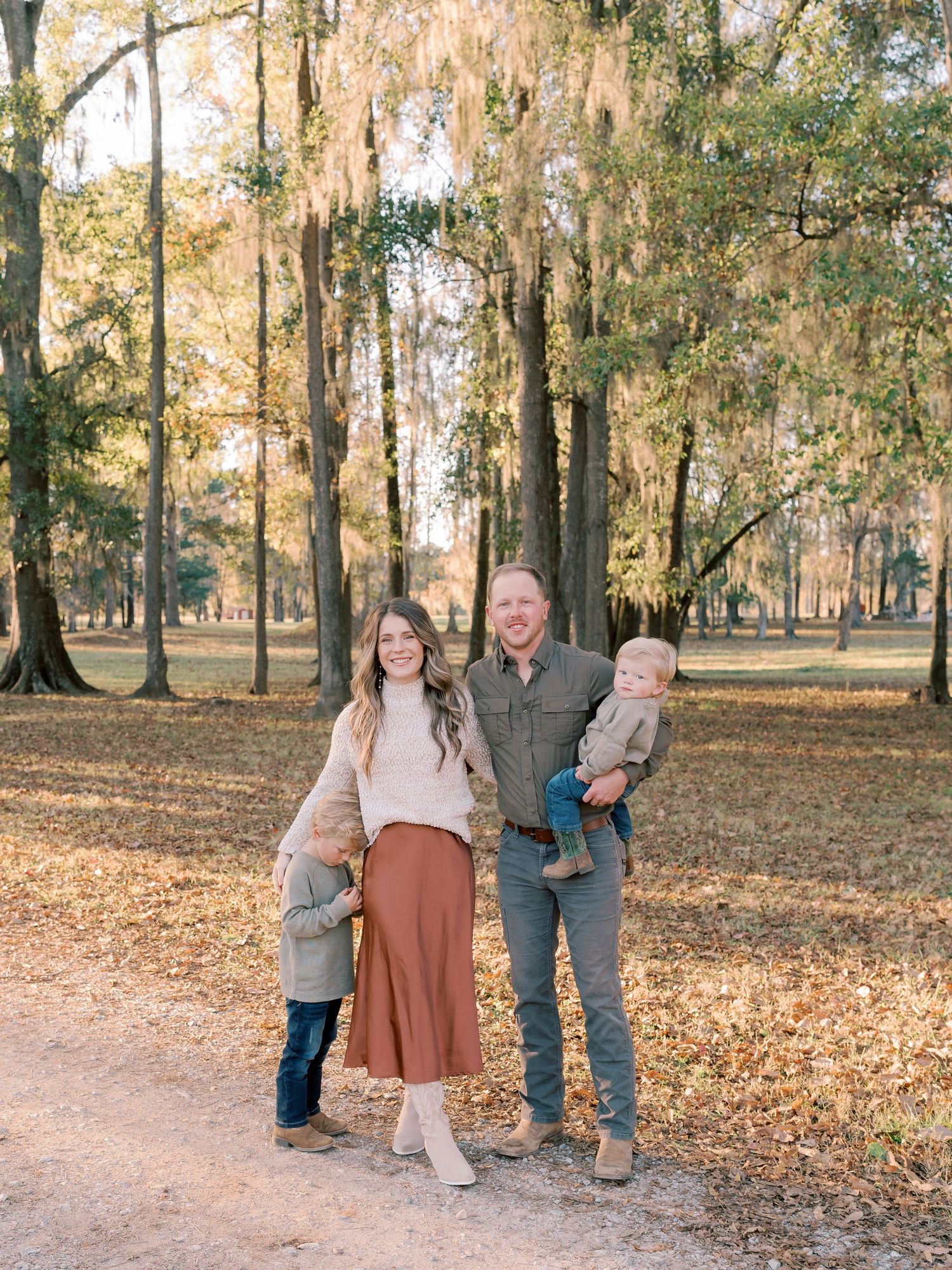 Family of four posing together on autumn path with Spanish moss hanging from trees.