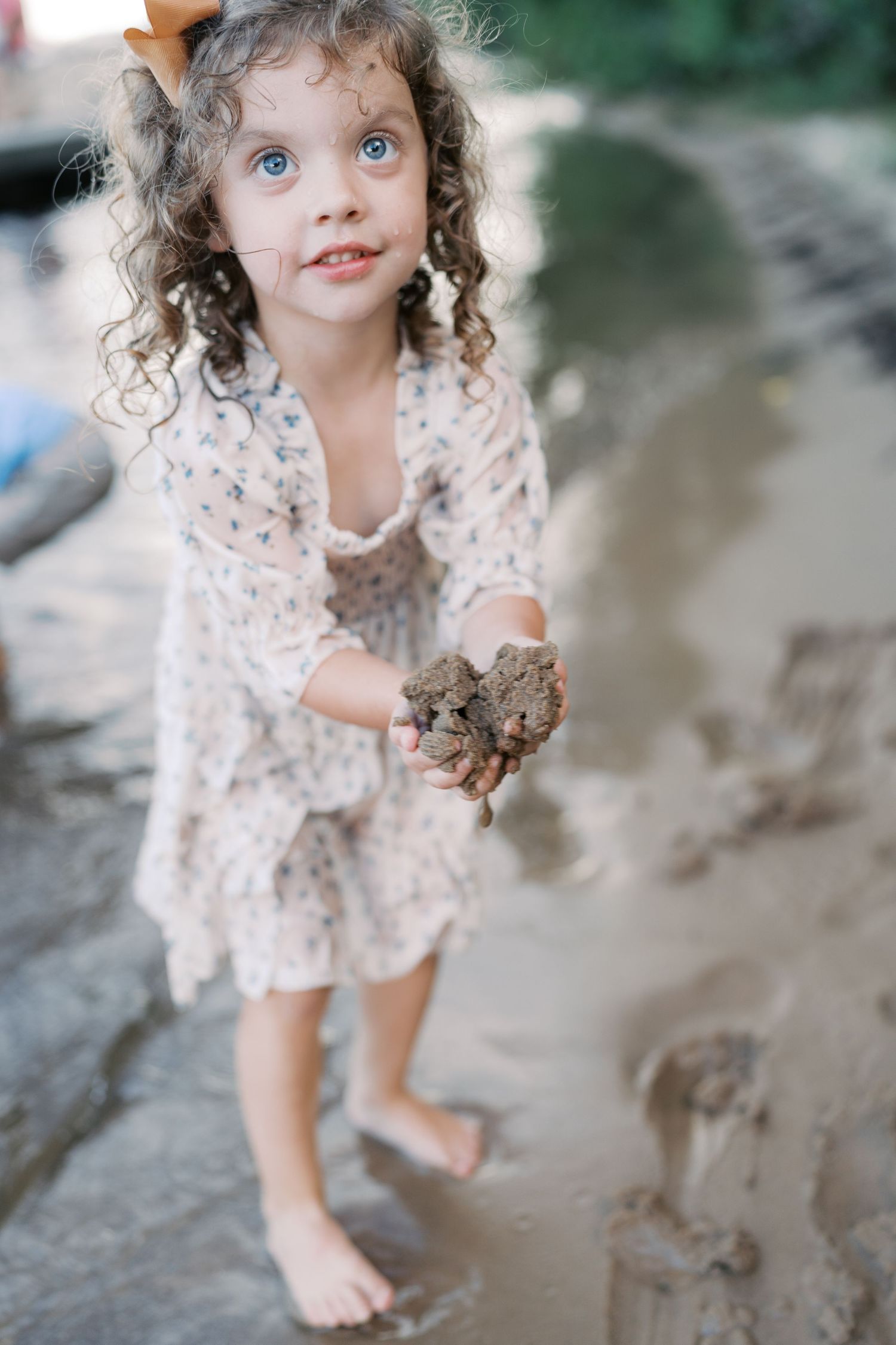 A child in a patterned dress plays in muddy water with joyful expression.