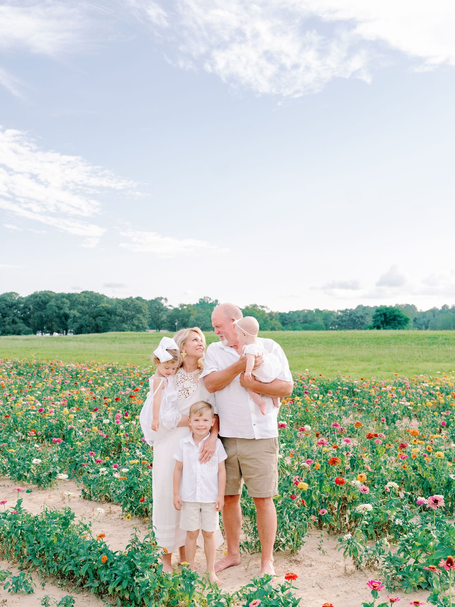 Family group poses candidly in a blooming flower field on a bright summer day.