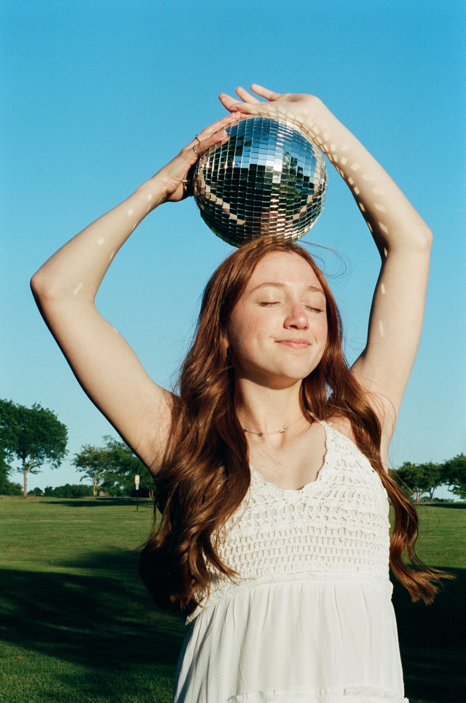 Playful outdoor photoshoot with a disco ball reflecting sunlight against bright blue sky.