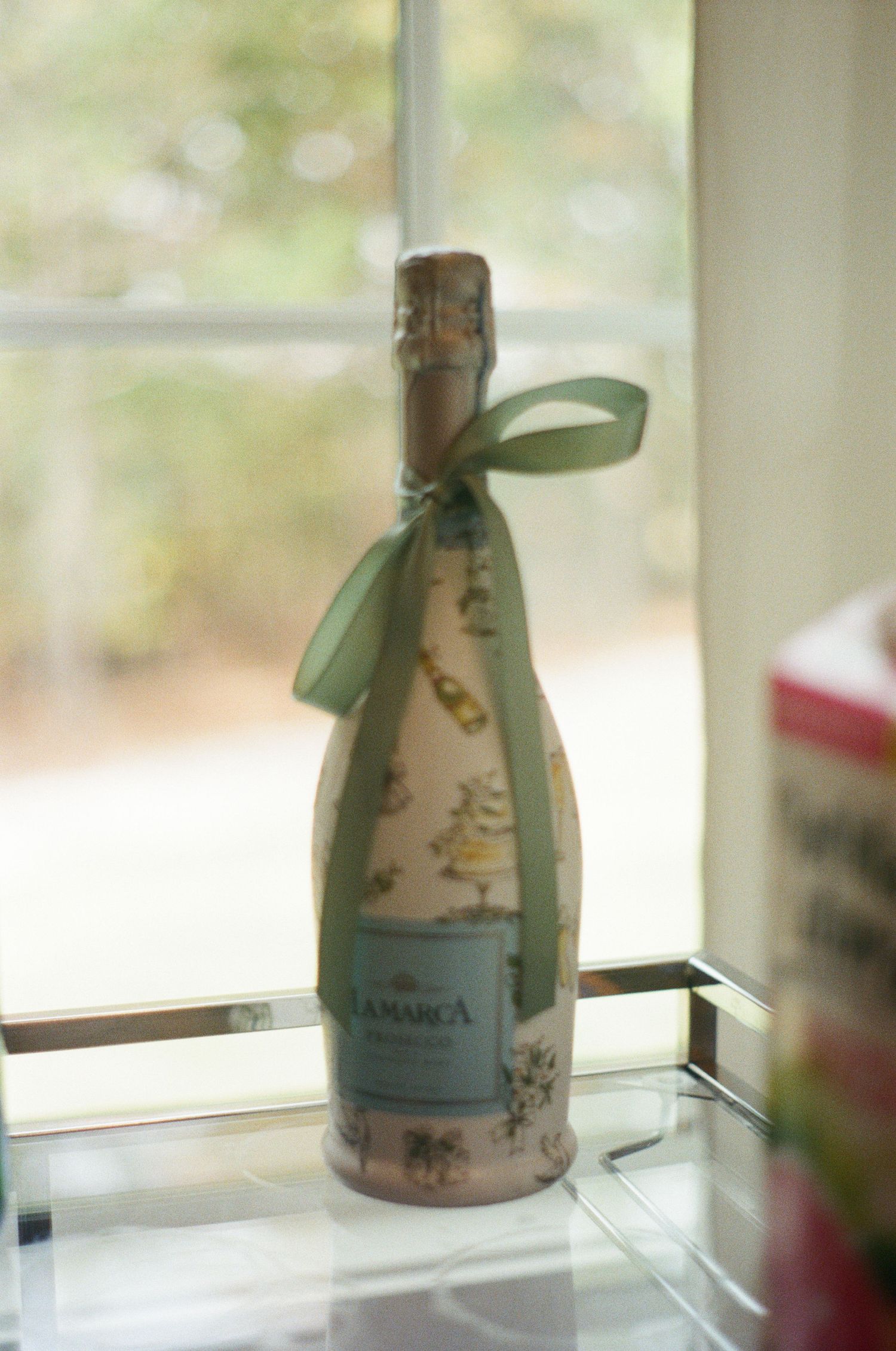 Decorative champagne bottle with green ribbon displayed on white surface.