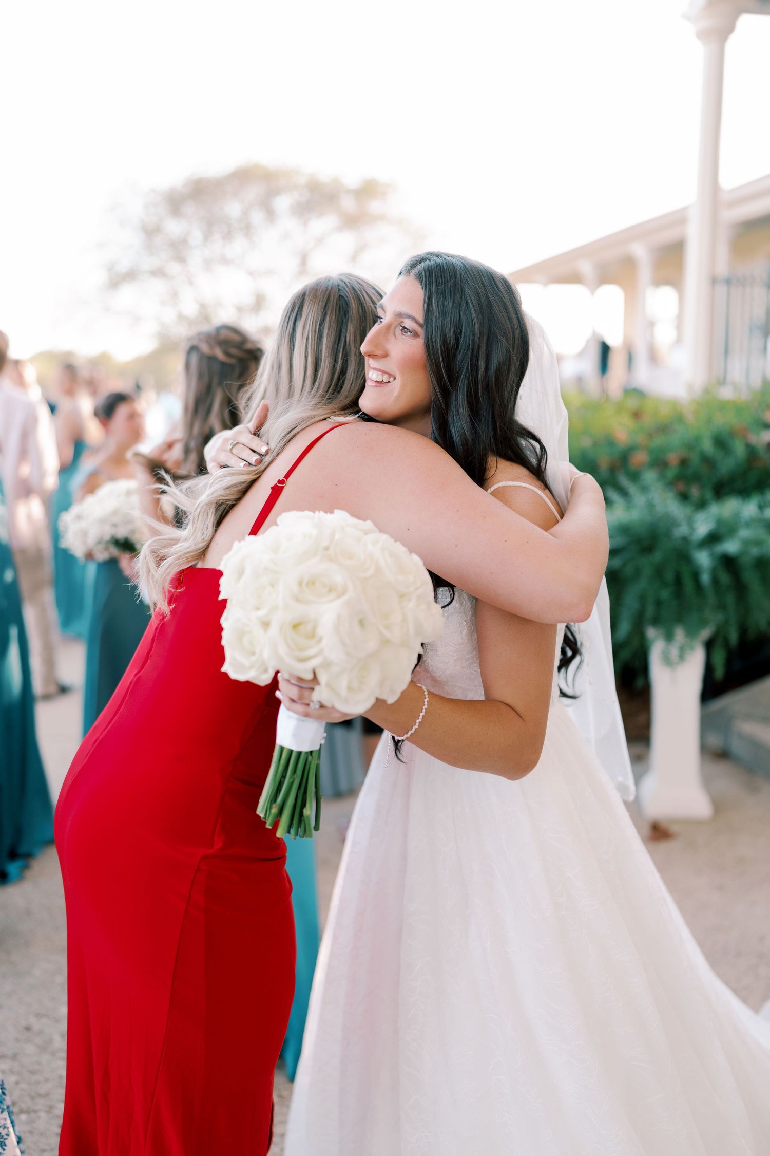 Emotional embrace between wedding attendees wearing red and white dresses holding white bouquets.