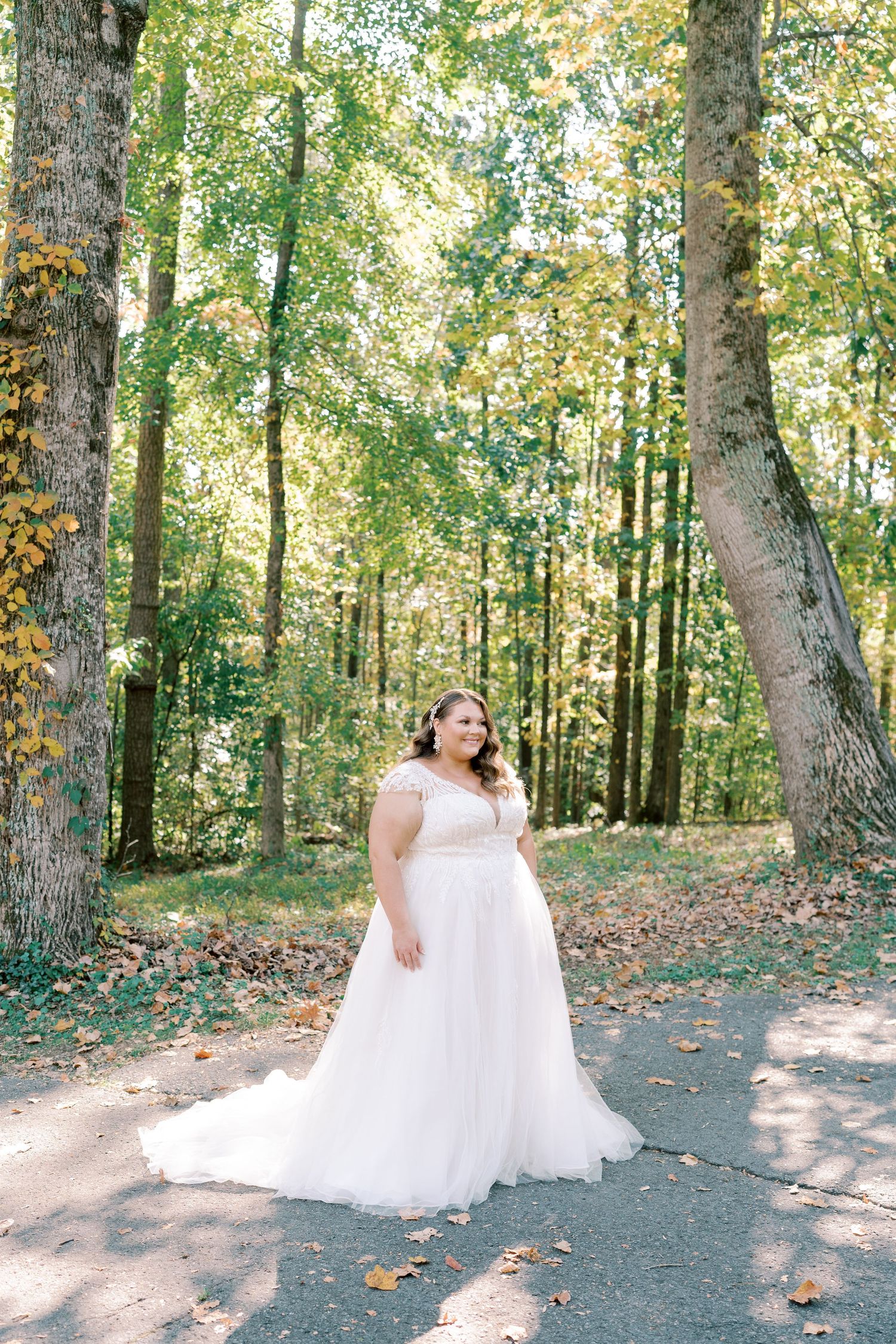 Bride in flowing white wedding gown twirling on outdoor path surrounded by trees.