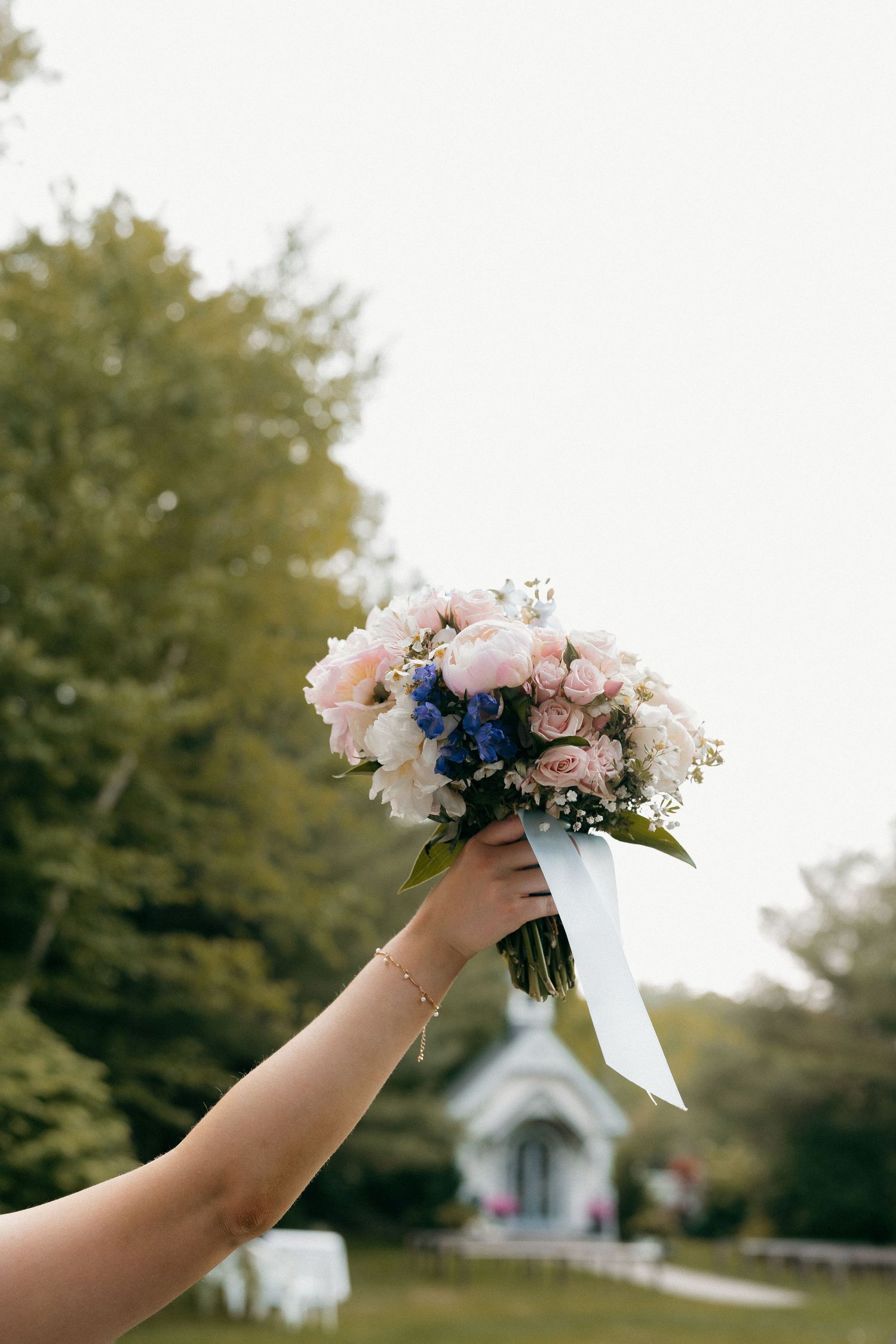 Hands holding up a delicate bridal bouquet with pink and white flowers against a chapel background.