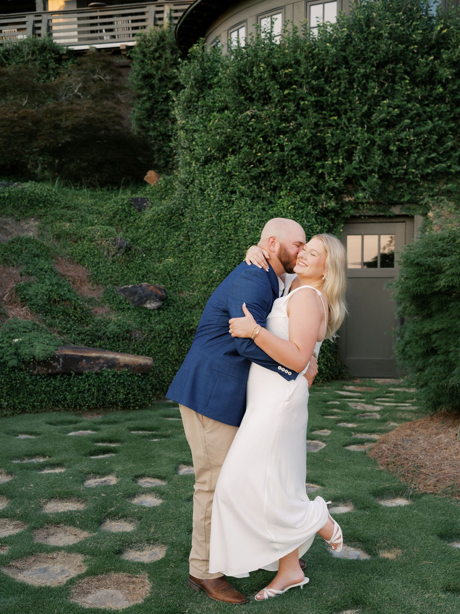 Couple dancing playfully on garden pathway surrounded by greenery.