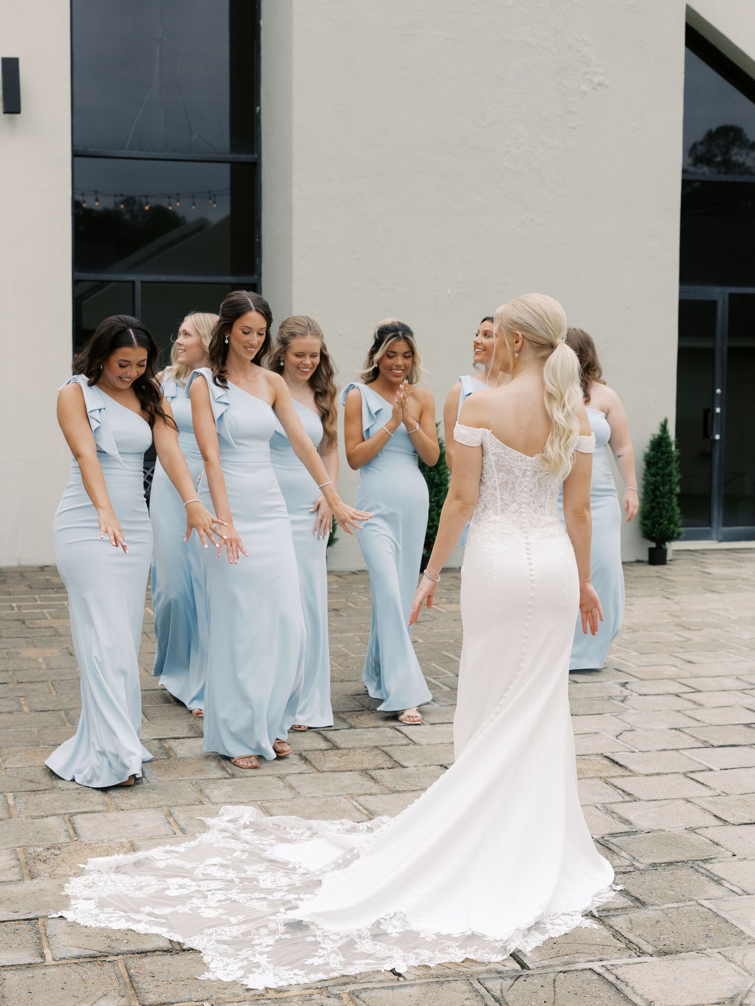 Bridesmaids in light blue dresses line up for a first look reveal with the bride in her white gown.