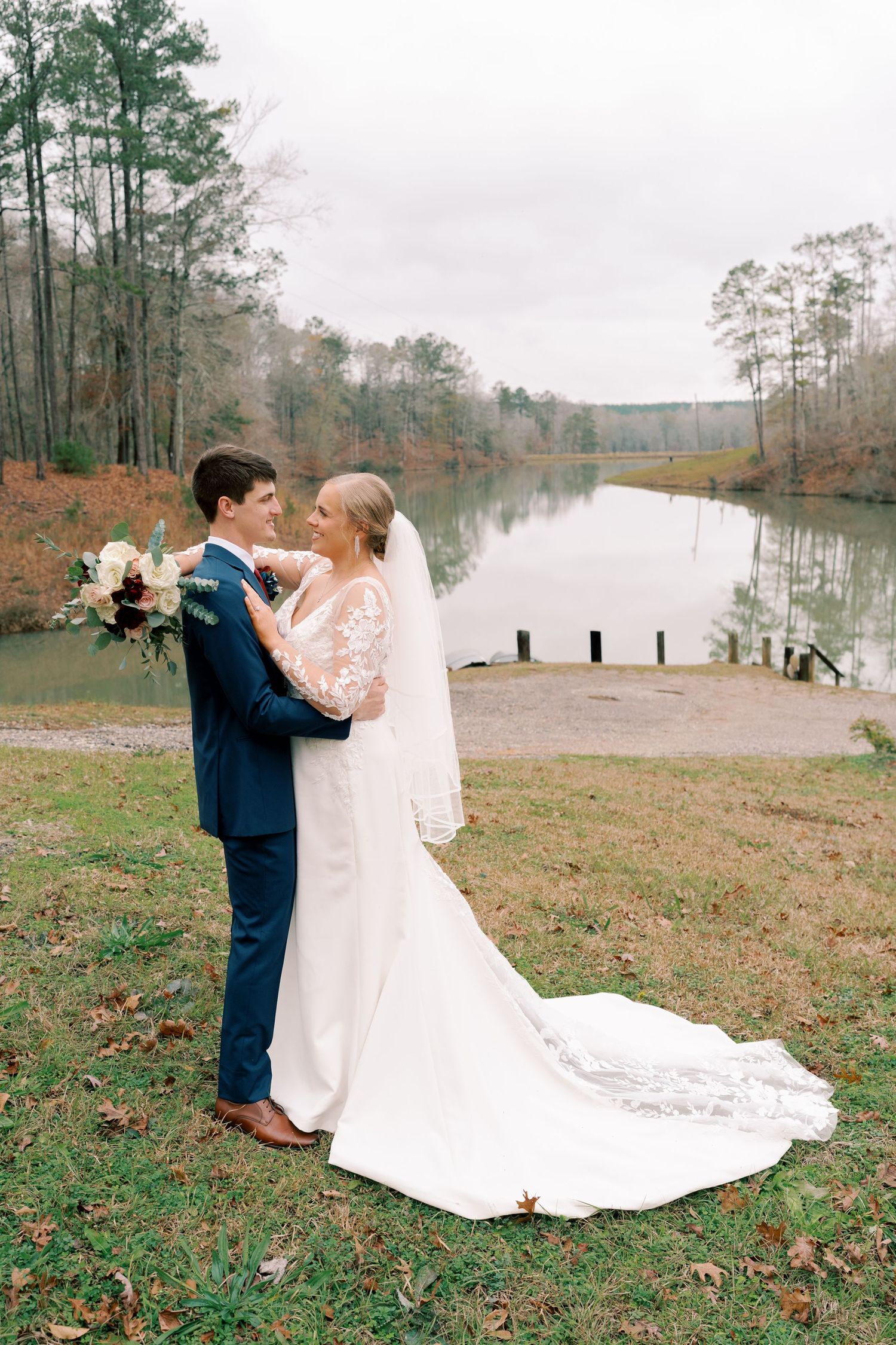 Wedding couple dances by lakeside on autumn day with fallen leaves.