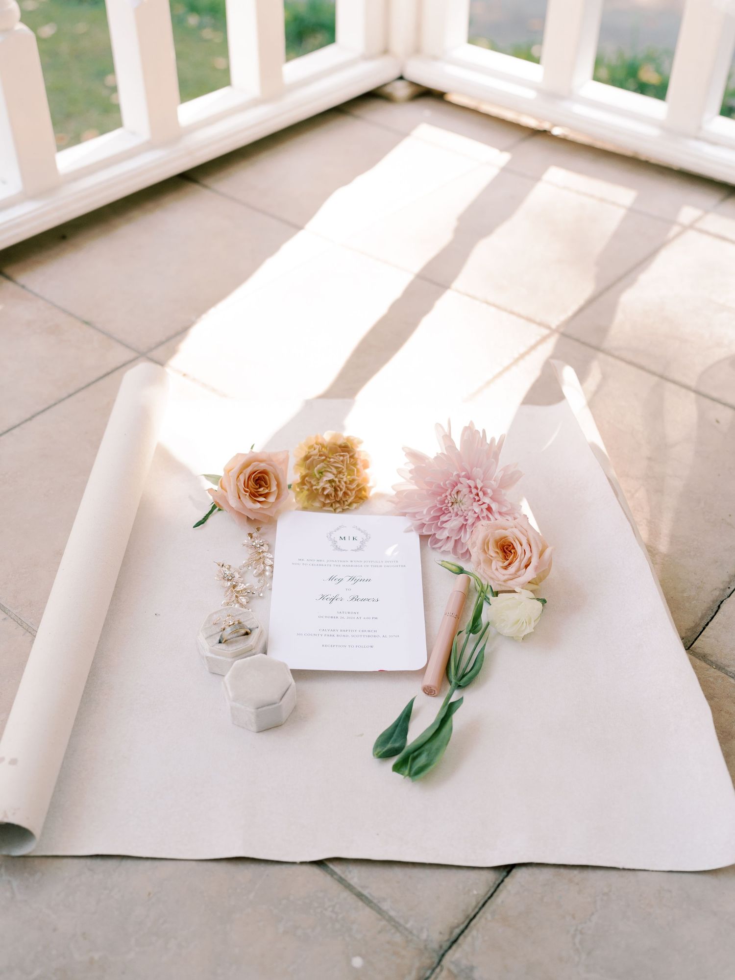 Wedding stationery and pink flowers arranged on white surface in natural light.