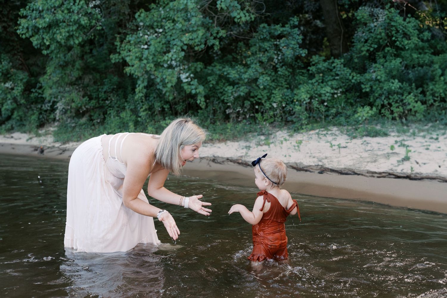 Family members enjoying playful moments in shallow river water near the shore.