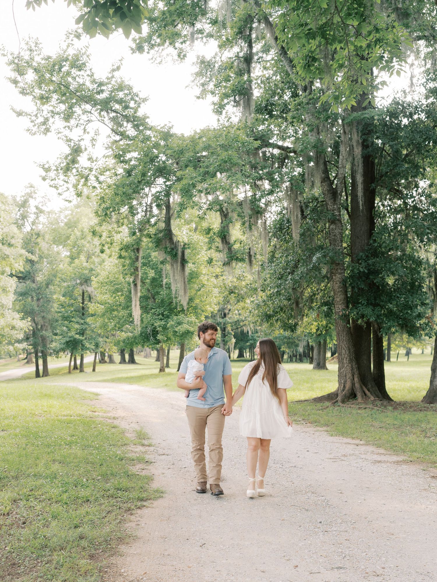 Three people walk hand in hand down a peaceful tree-lined trail in a park.