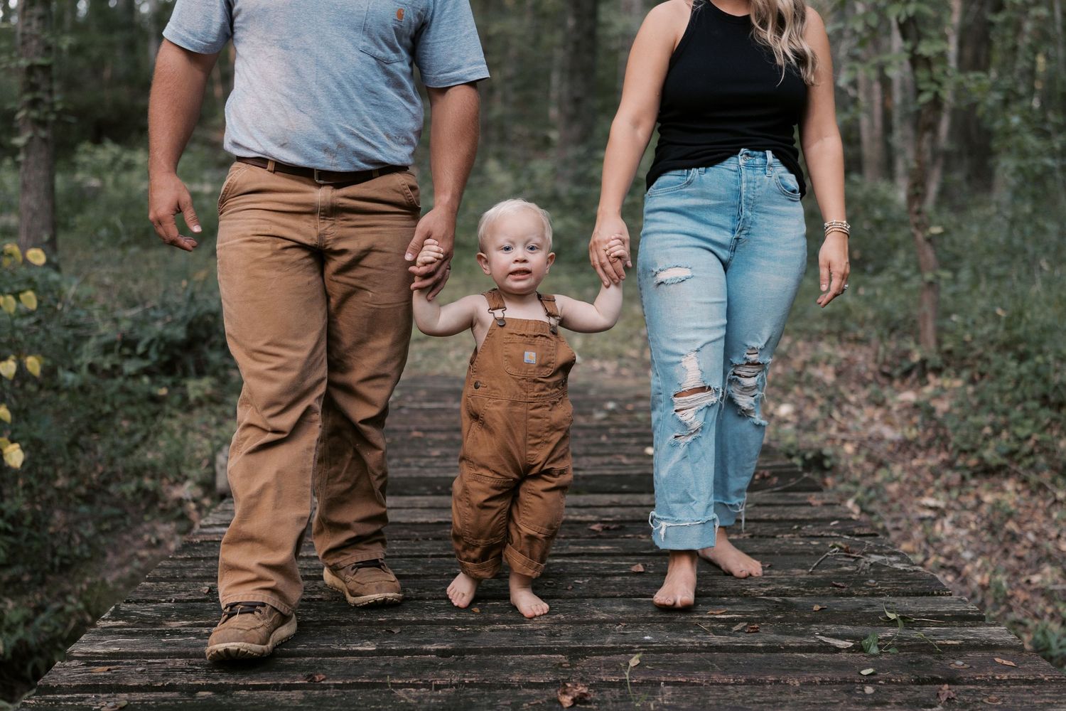 Family members walk together on a rustic wooden bridge surrounded by trees.