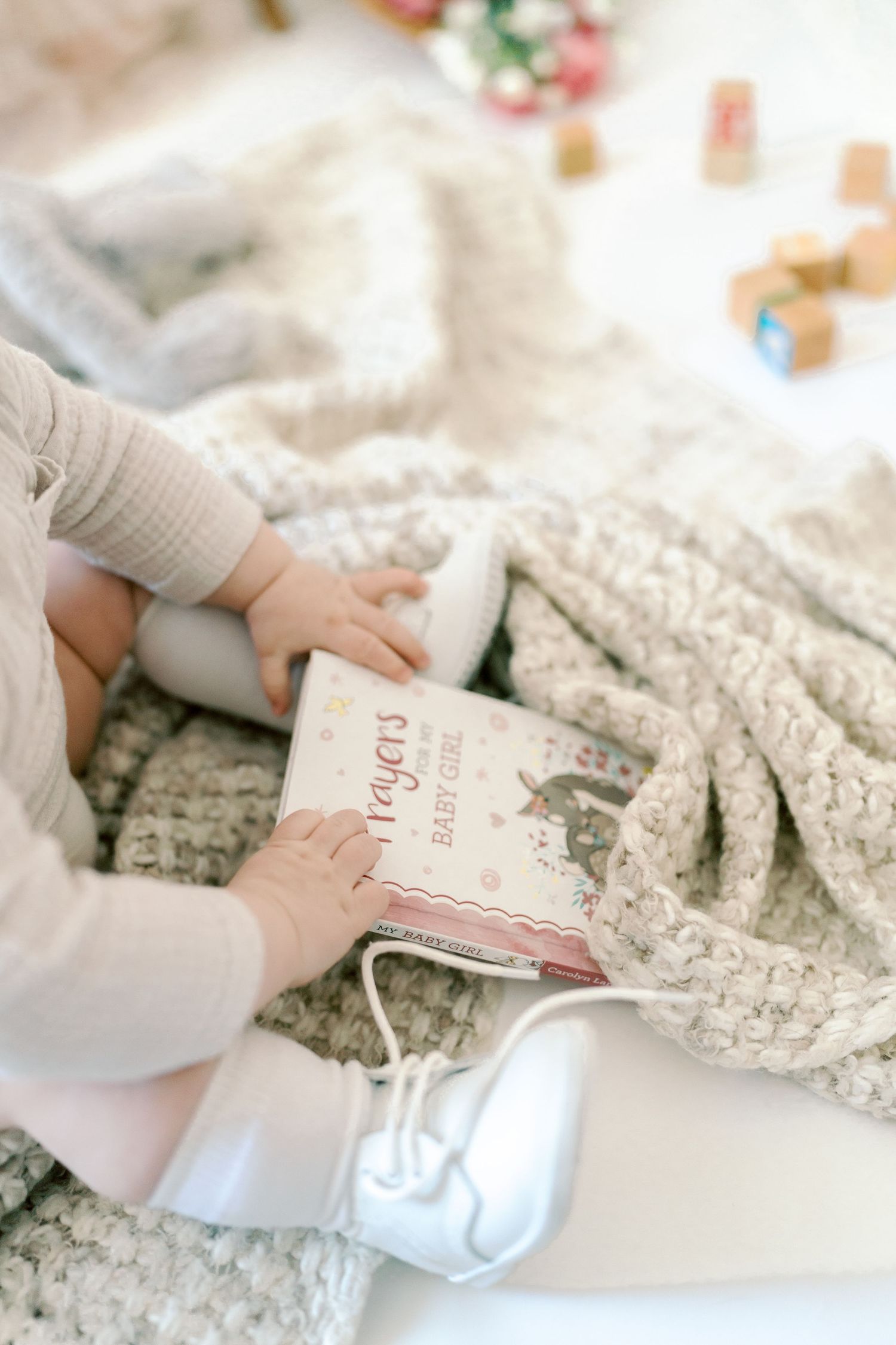 Close-up of tiny hands touching lace fabric and book pages on white surface.