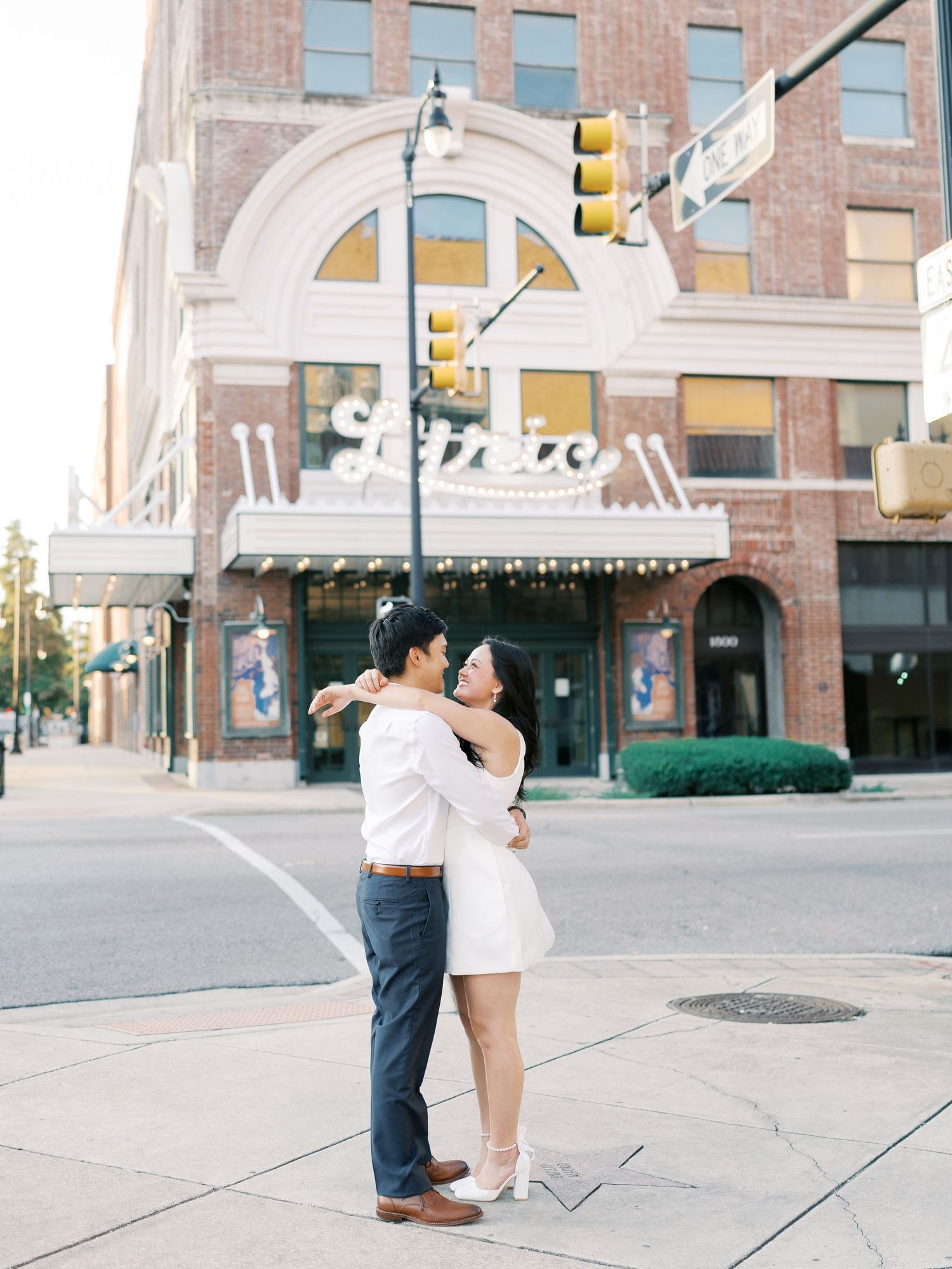 A couple embraces while dancing on a downtown sidewalk near brick buildings.