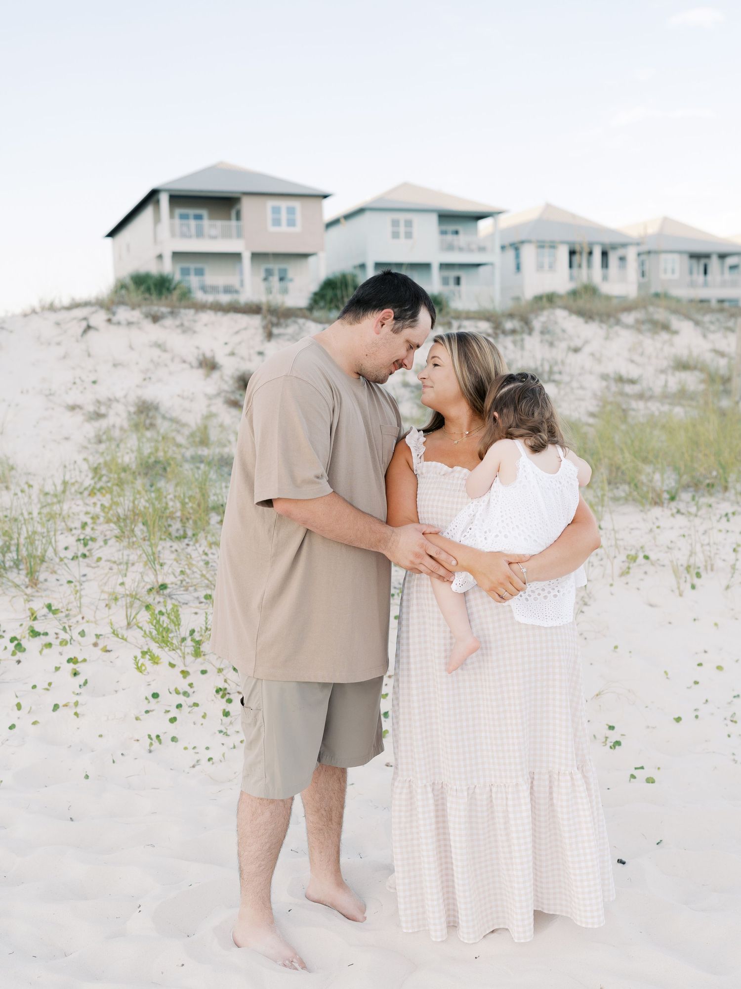 Intimate family portrait session on white sandy beach with beach houses visible in background.
