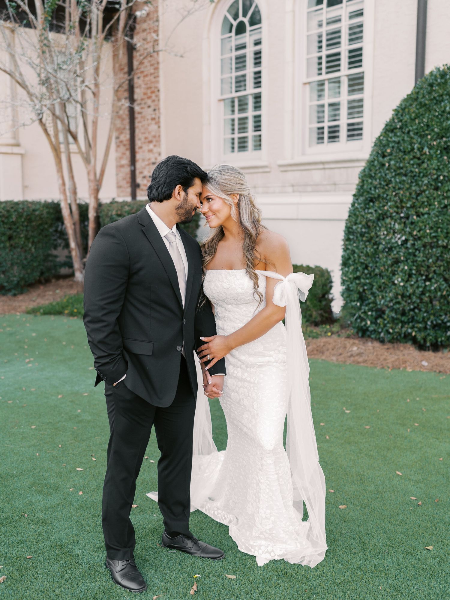 Elegant outdoor wedding portraits on a manicured lawn with classic architecture in background.
