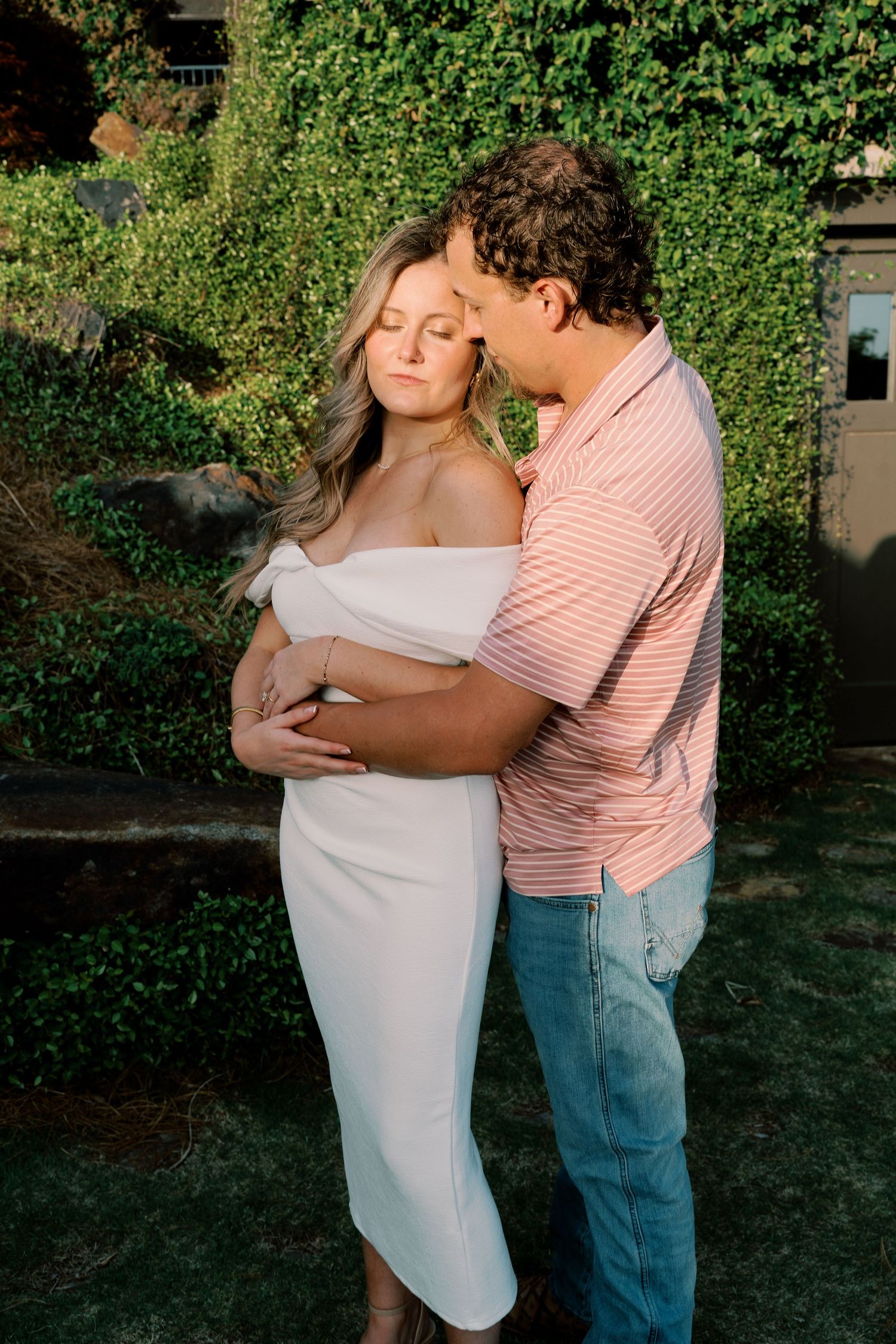 A couple shares an intimate moment in a garden setting at sunset.