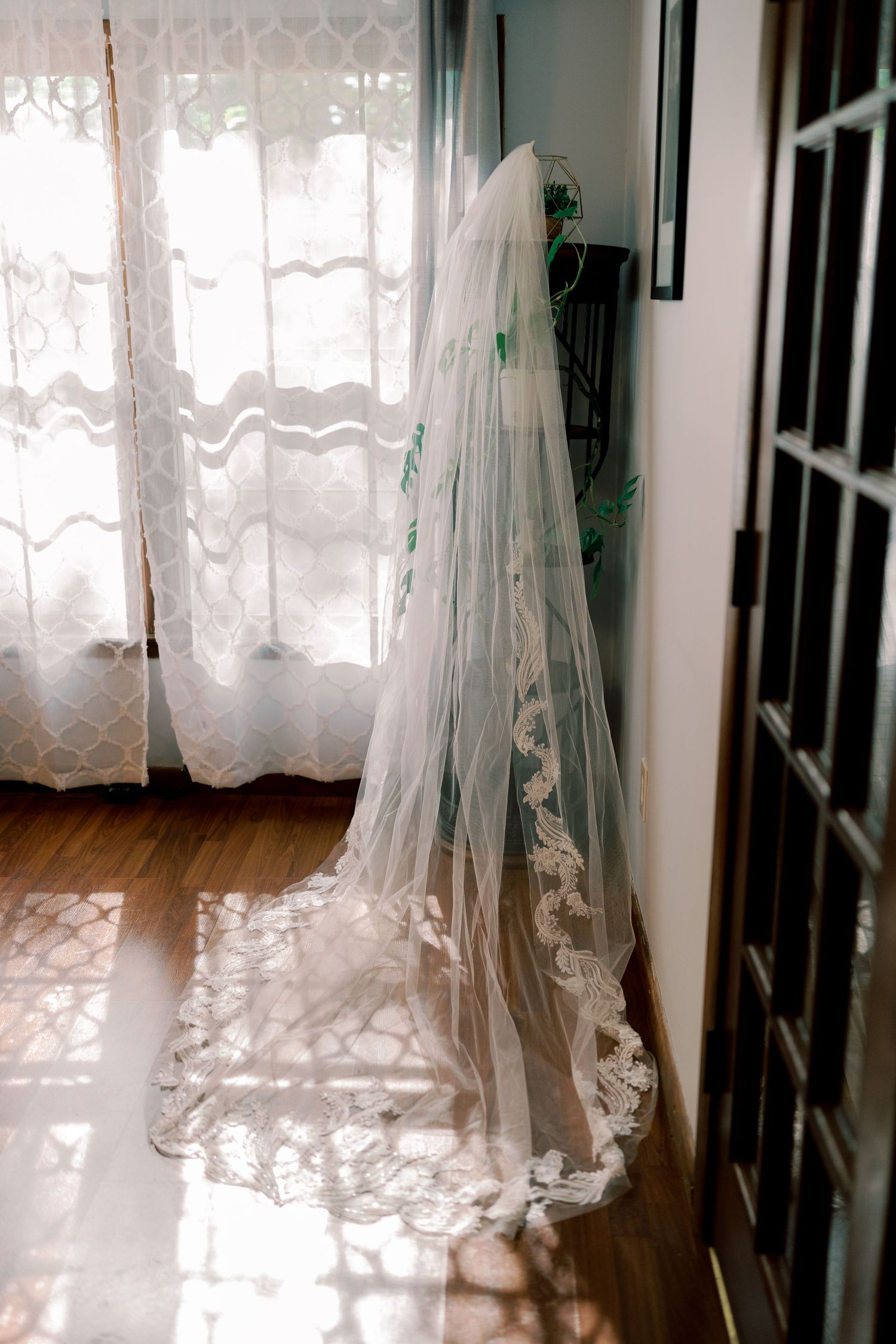 Lace-trimmed wedding veil hanging by window with sunlight casting intricate shadows.