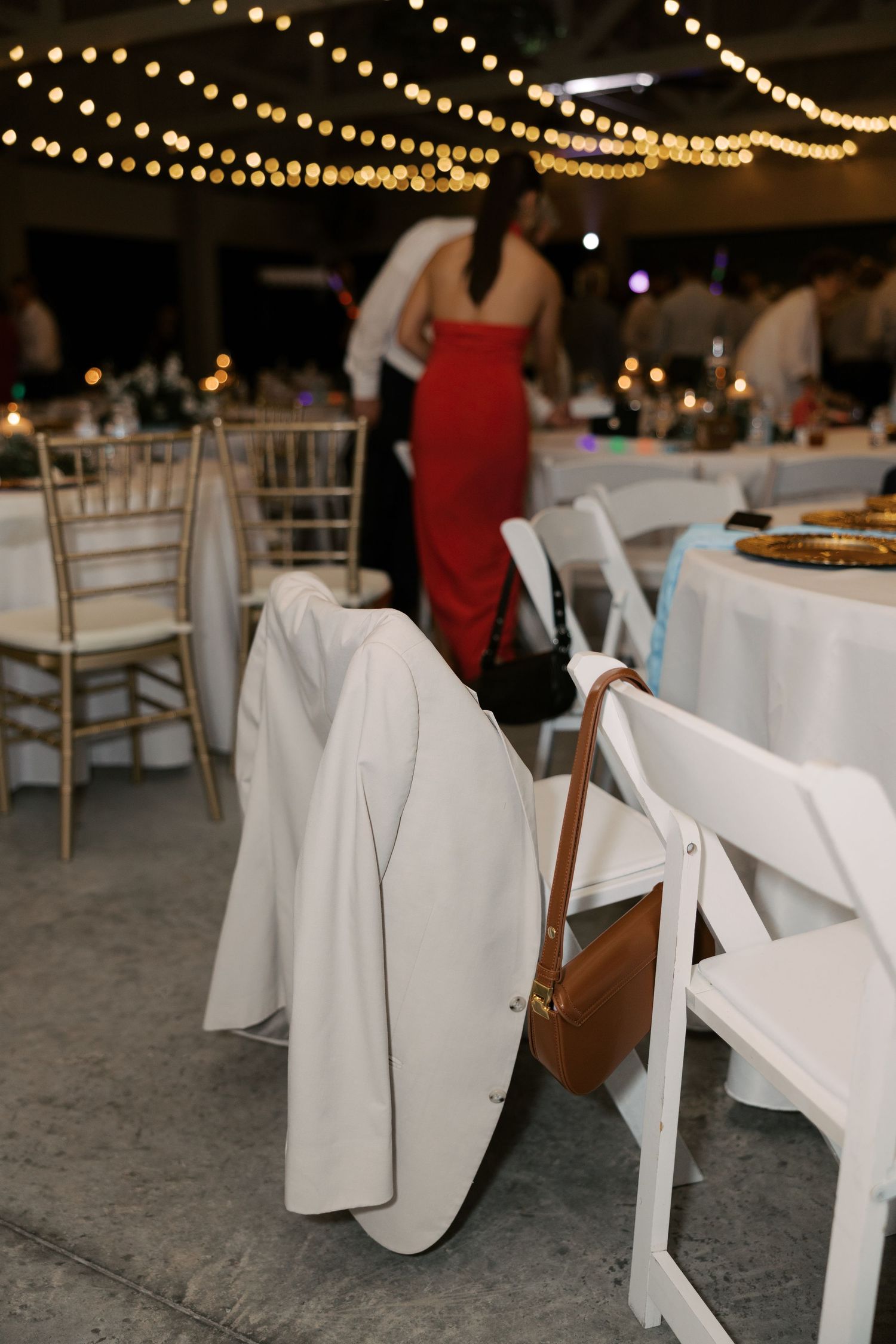 White folding chairs with elegant linens arranged at a wedding reception under string lights.