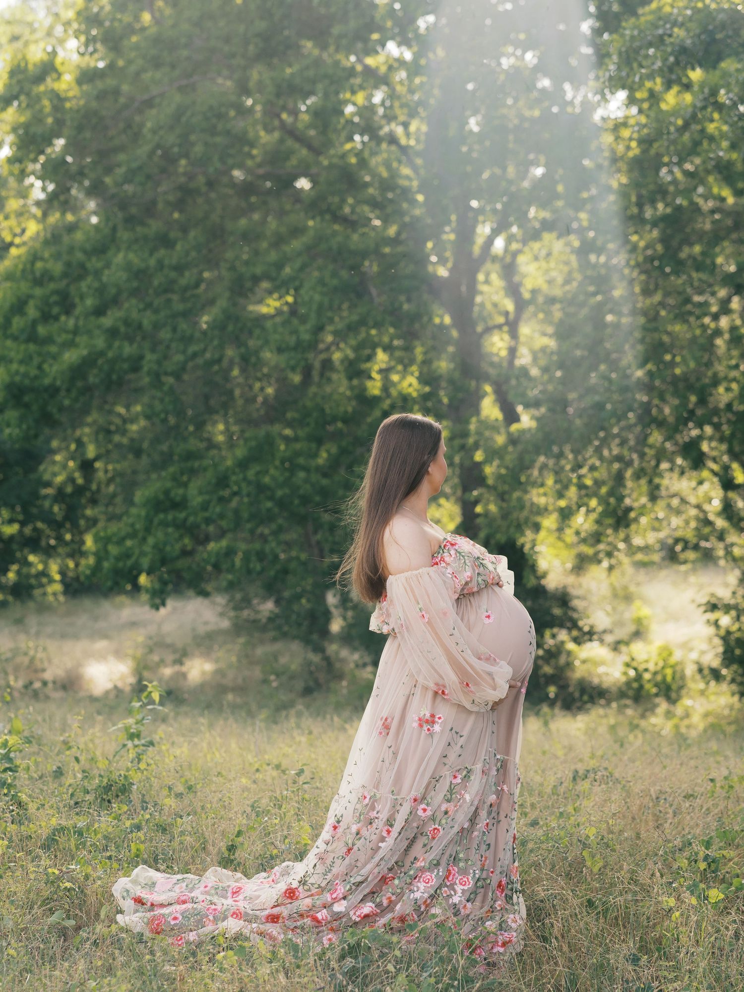 Ethereal pink floral dress flows in a sunlit meadow with golden grass and green trees.