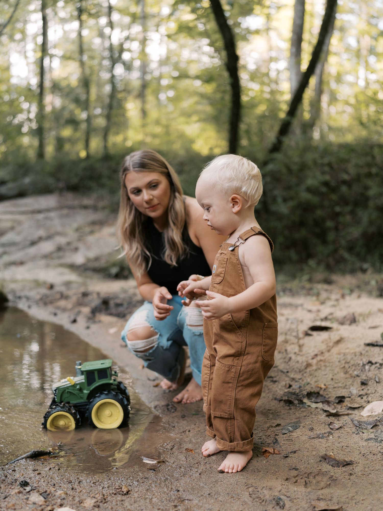 A family plays with toys on a dirt path near a stream in the woods.