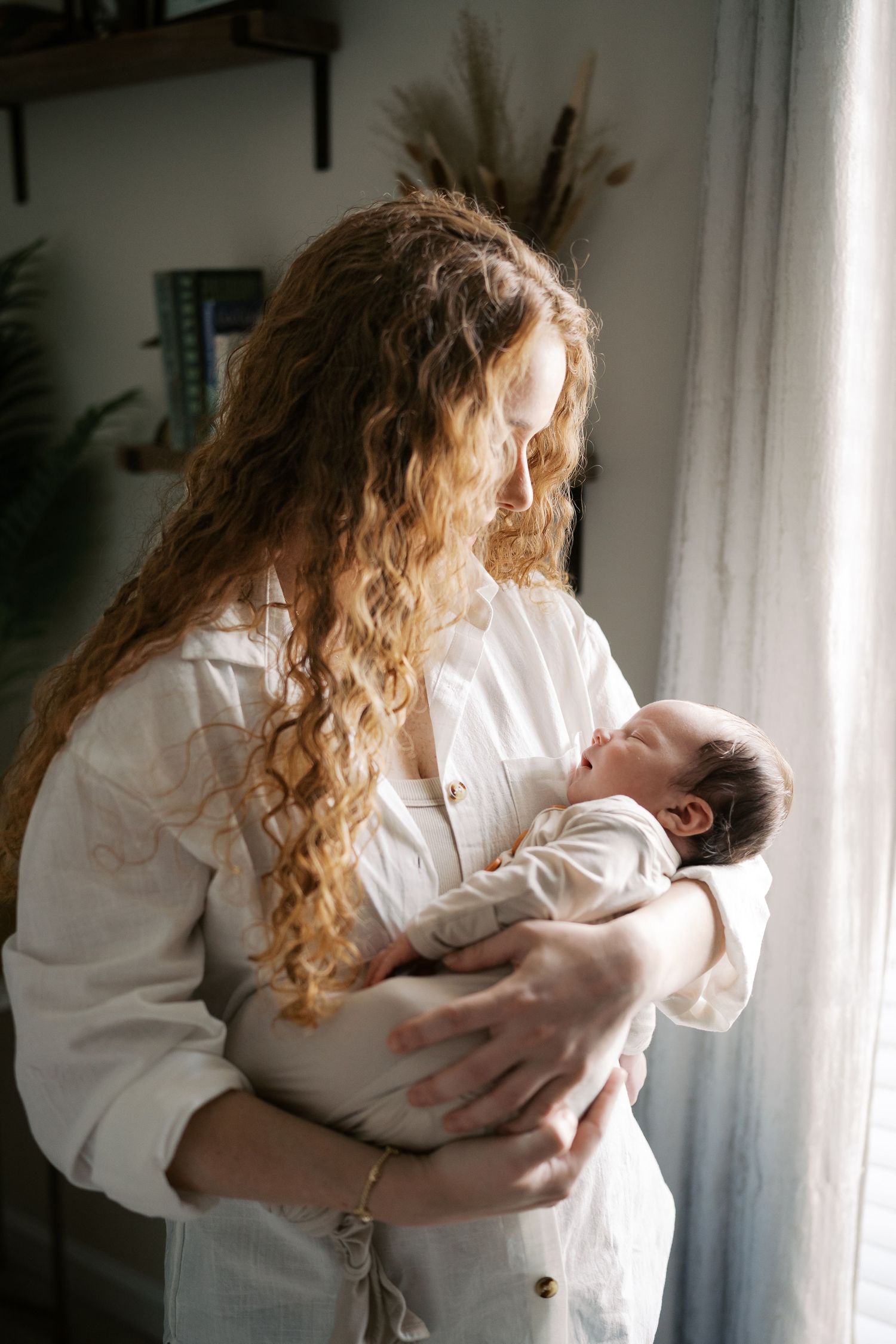 Gentle moments captured in natural light show a baby being held in a white button-down shirt.