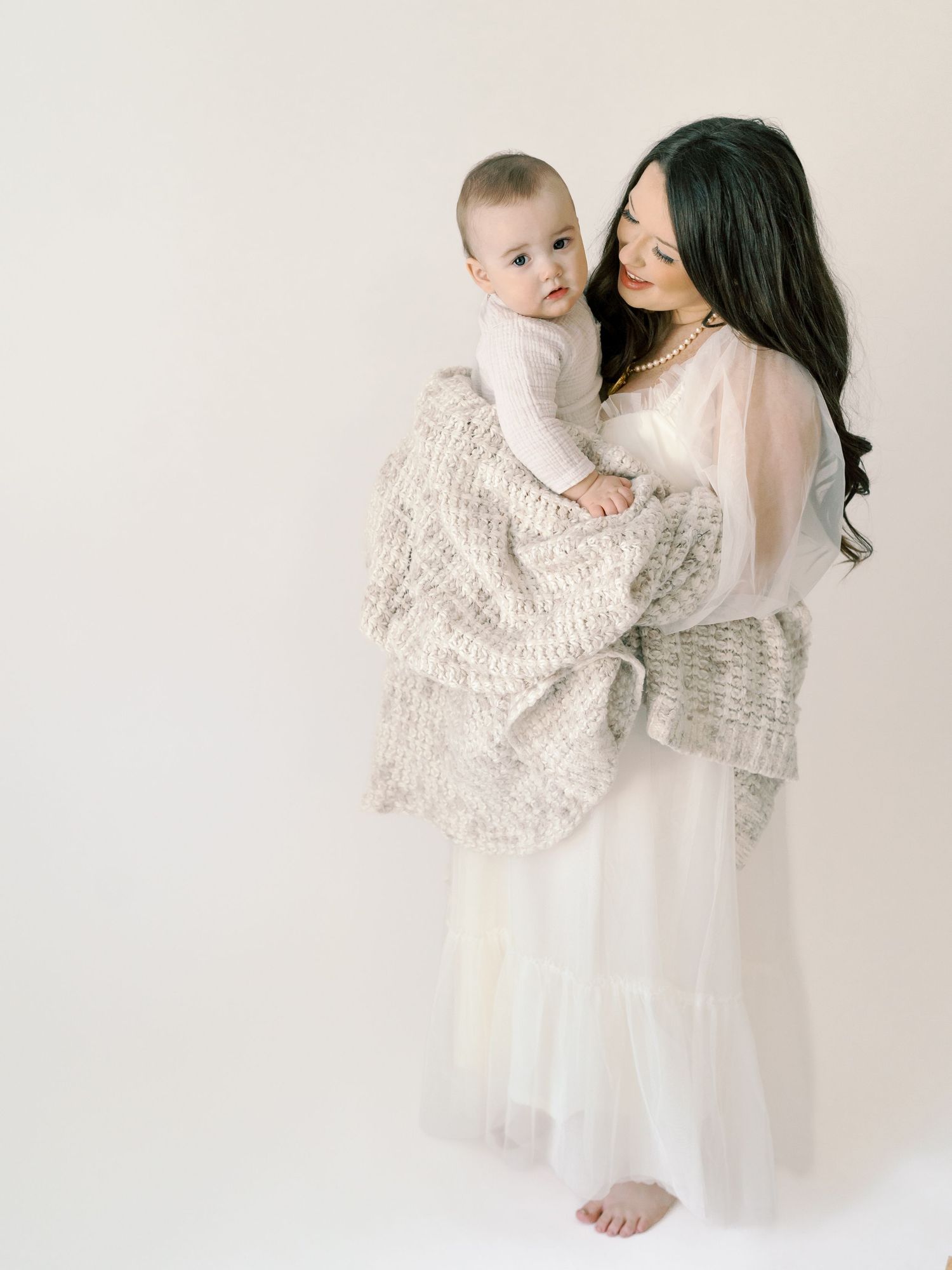 Mother and baby wearing matching white outfits in minimalist studio setting.