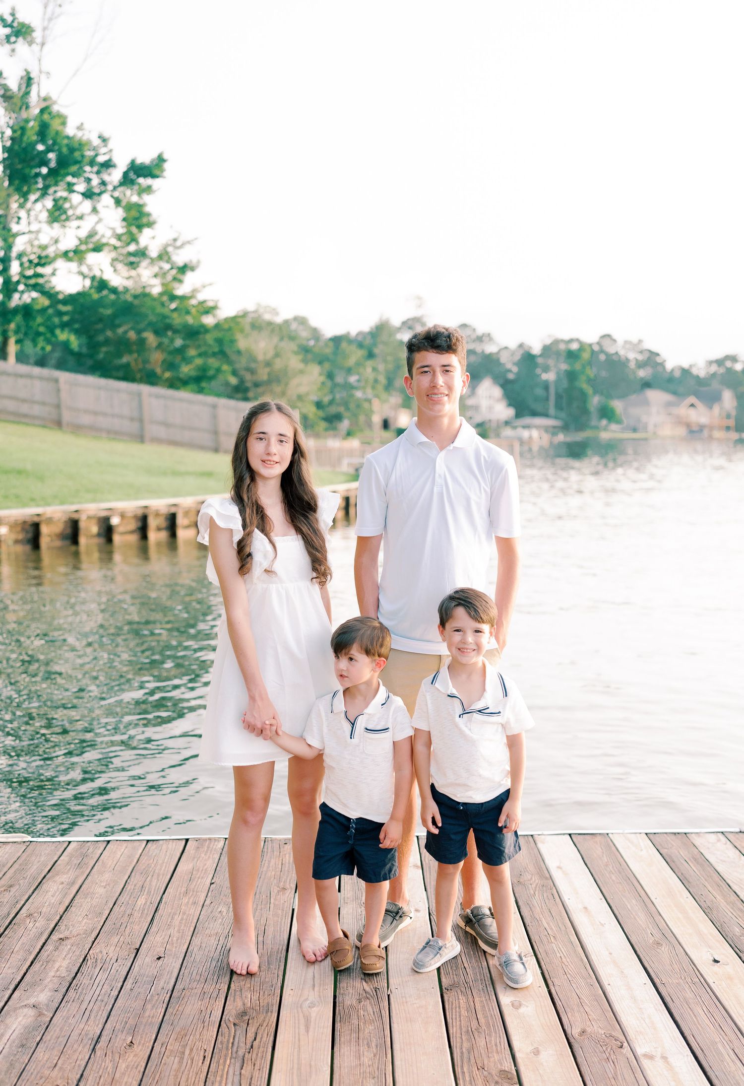 Family in coordinated white outfits poses together on lakeside wooden dock.
