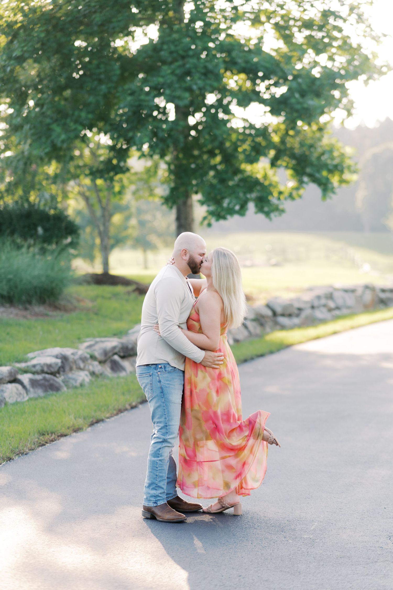 Romantic couple sharing tender moment on path surrounded by greenery and stone wall.