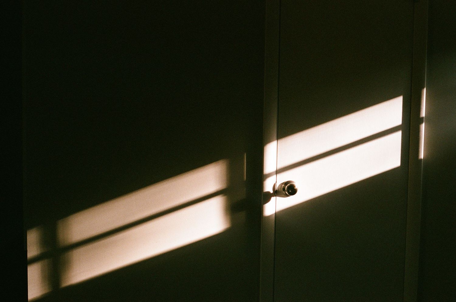 Bright sunlight casts geometric shadows through a window onto an interior wall.