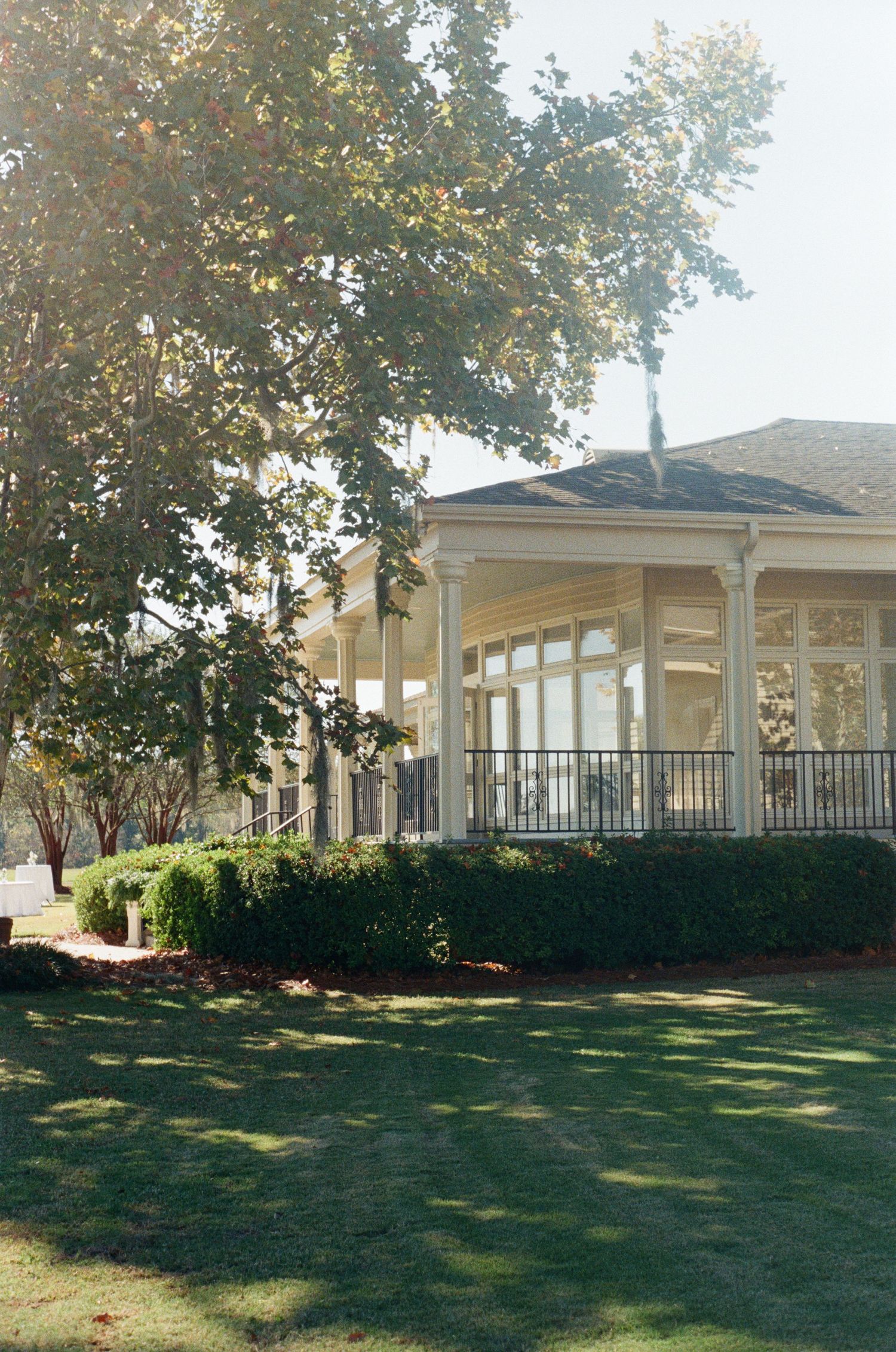 Elegant white wedding venue with columns and wraparound porch on landscaped grounds.