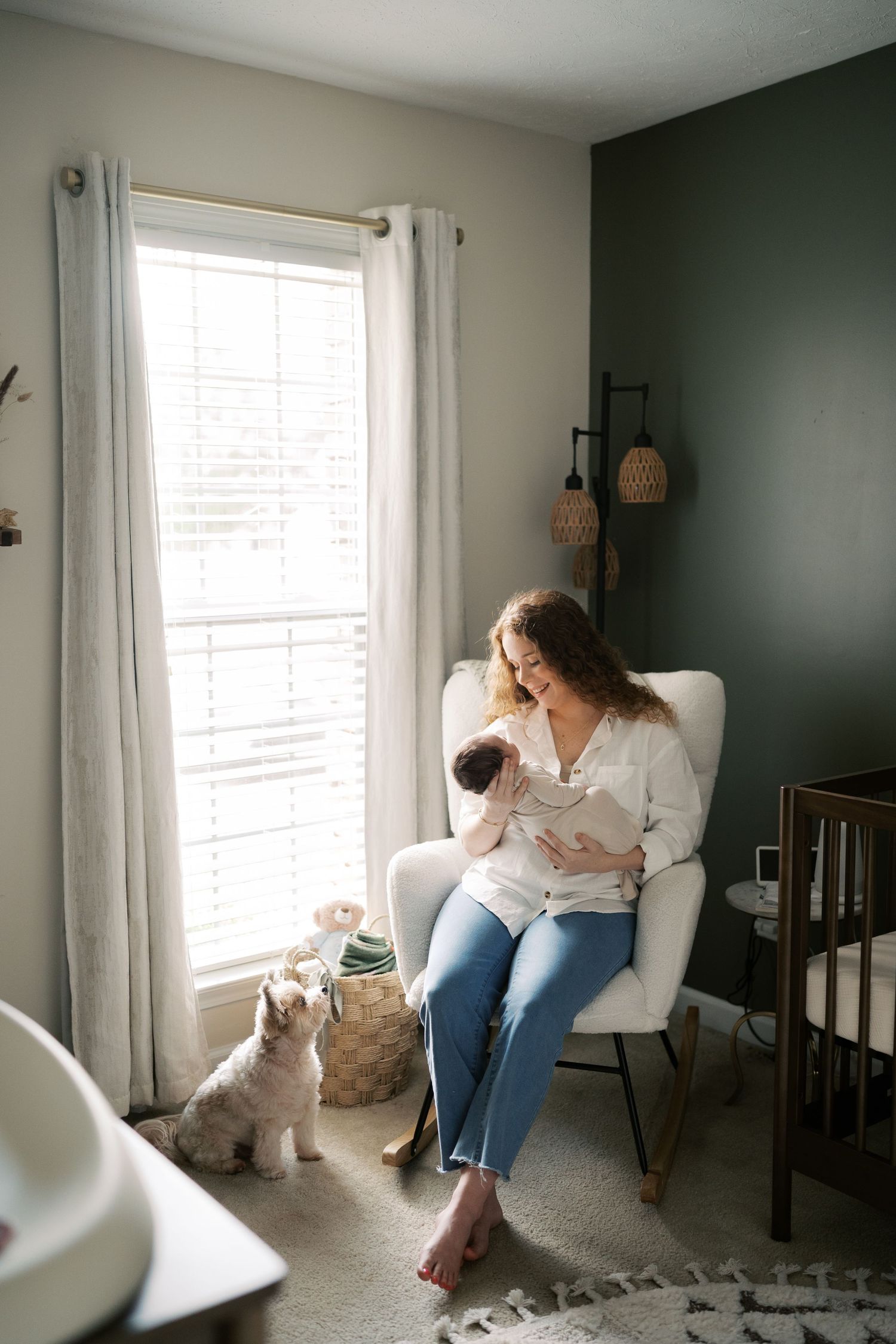 A peaceful nursery scene with white curtains and a dark accent wall features a rocking chair by the window.