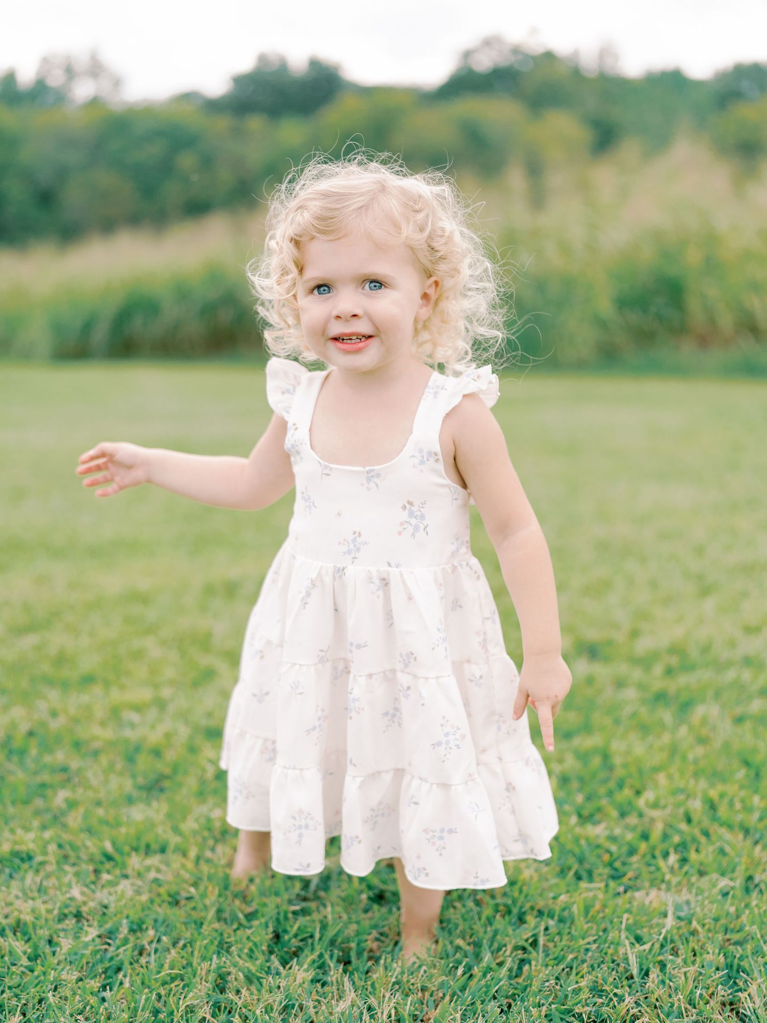 Playful toddler in white eyelet dress running through green summer field.