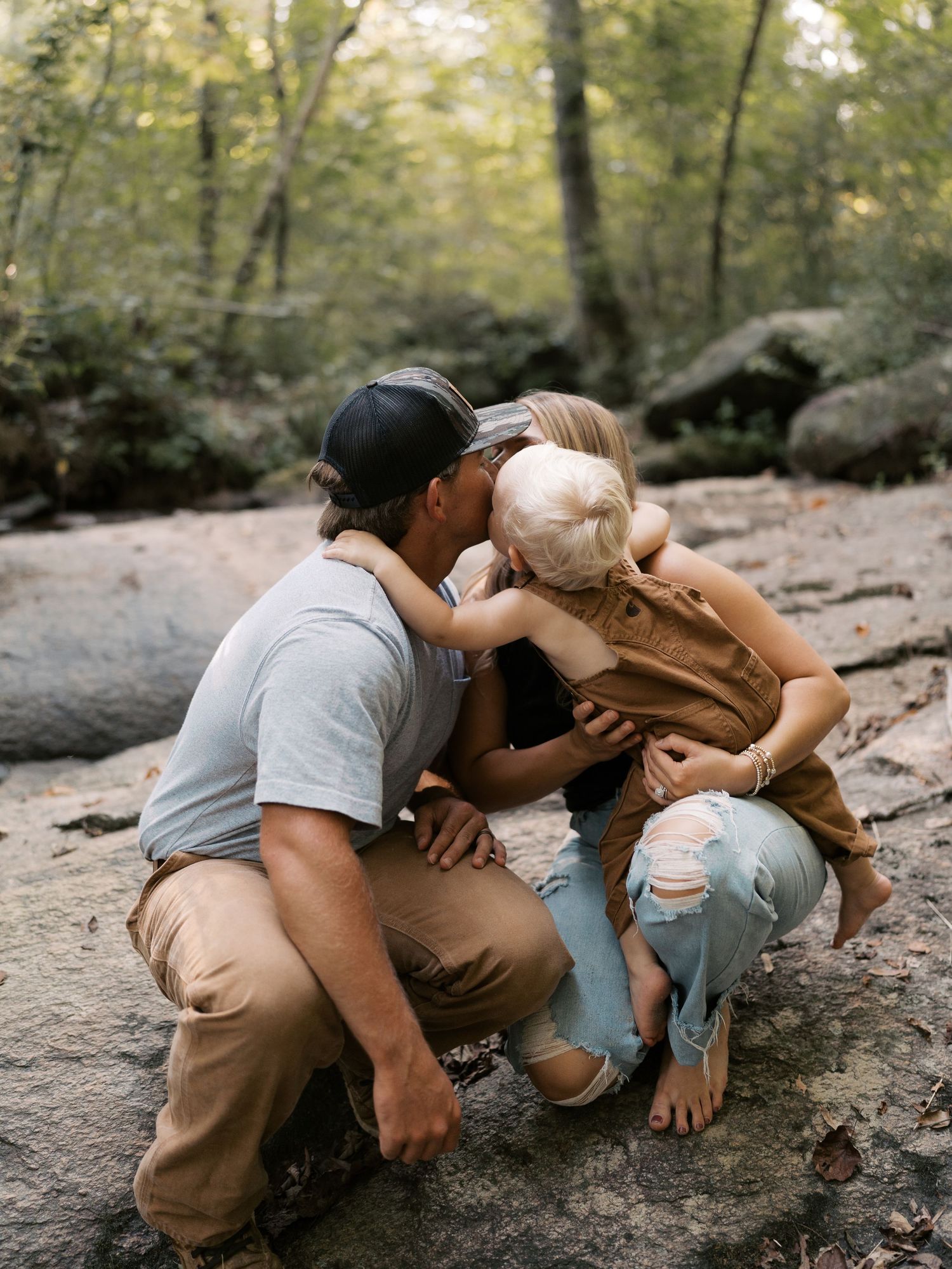 A family shares playful moments while sitting on the ground in a wooded area.