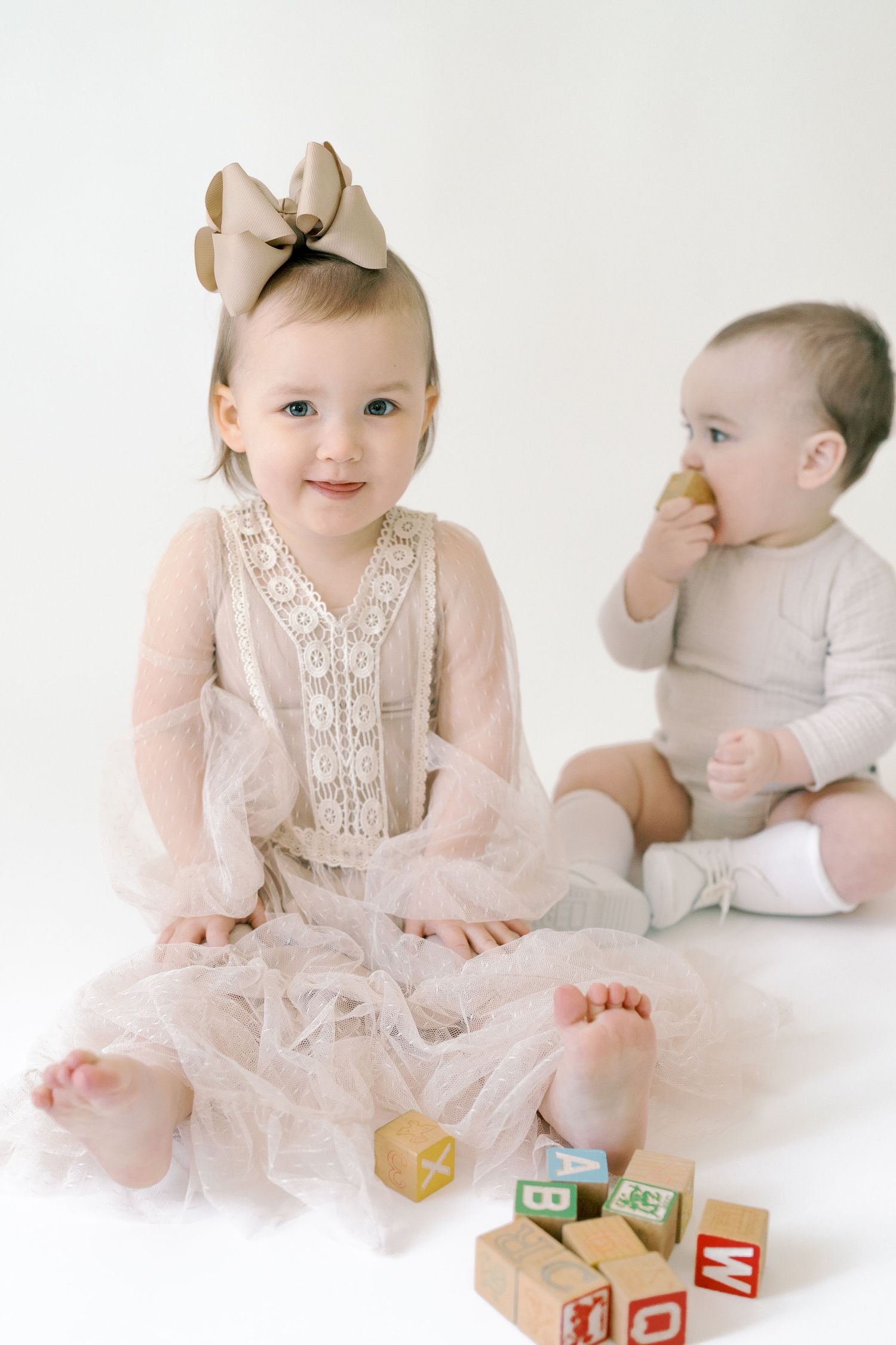 Two babies in vintage-style outfits playing with wooden alphabet blocks on white background.
