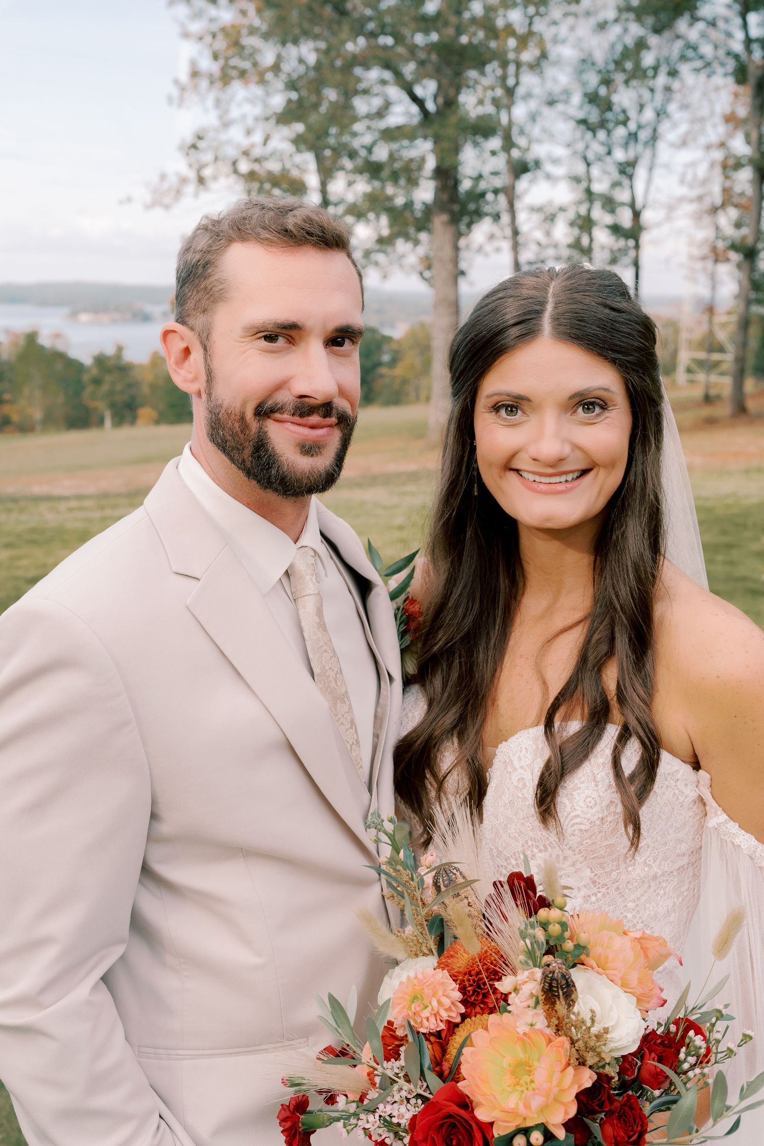Wedding couple poses together outdoors with a beautiful fall-colored floral bouquet.