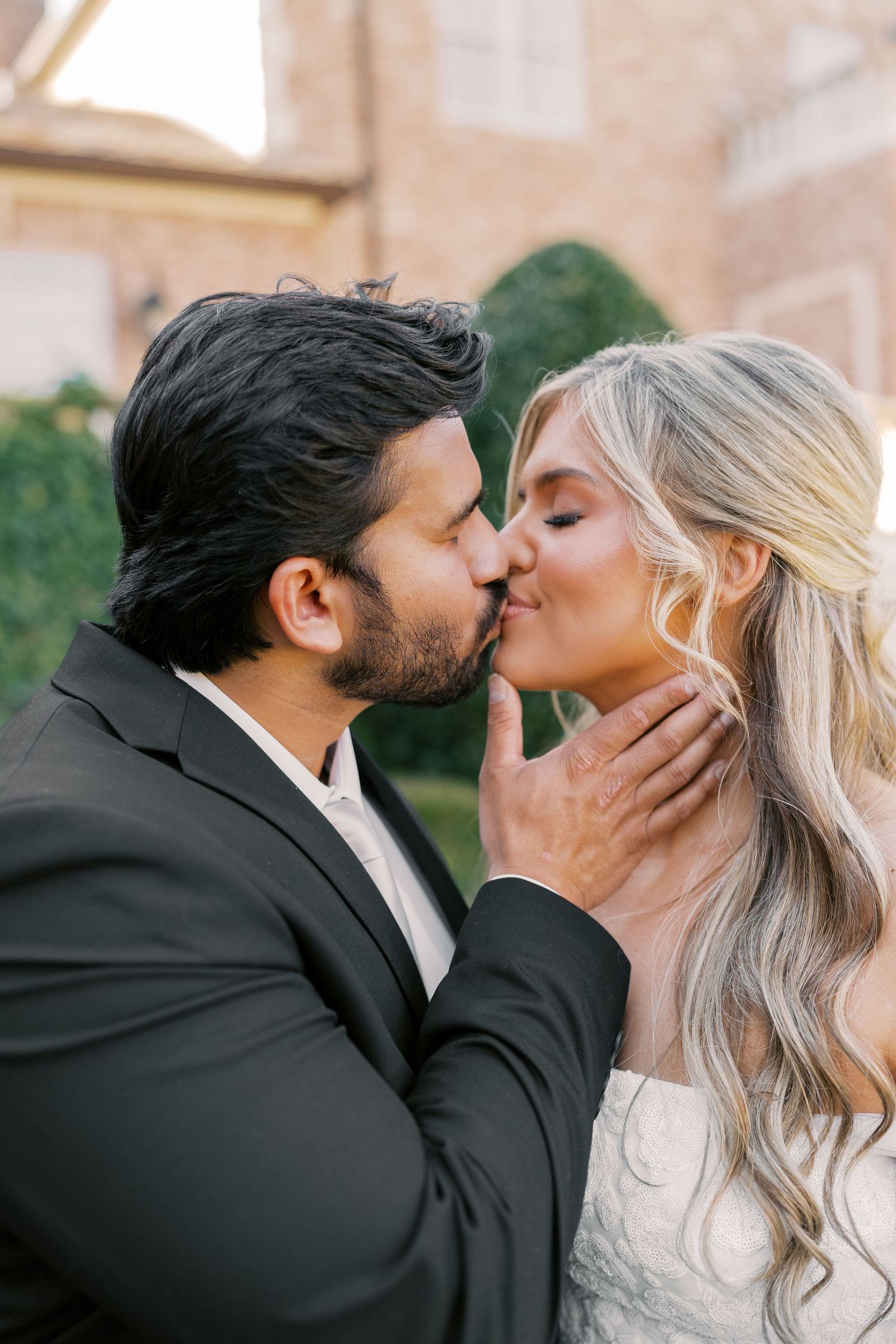An intimate kiss shared between a couple outside a stately brick building.